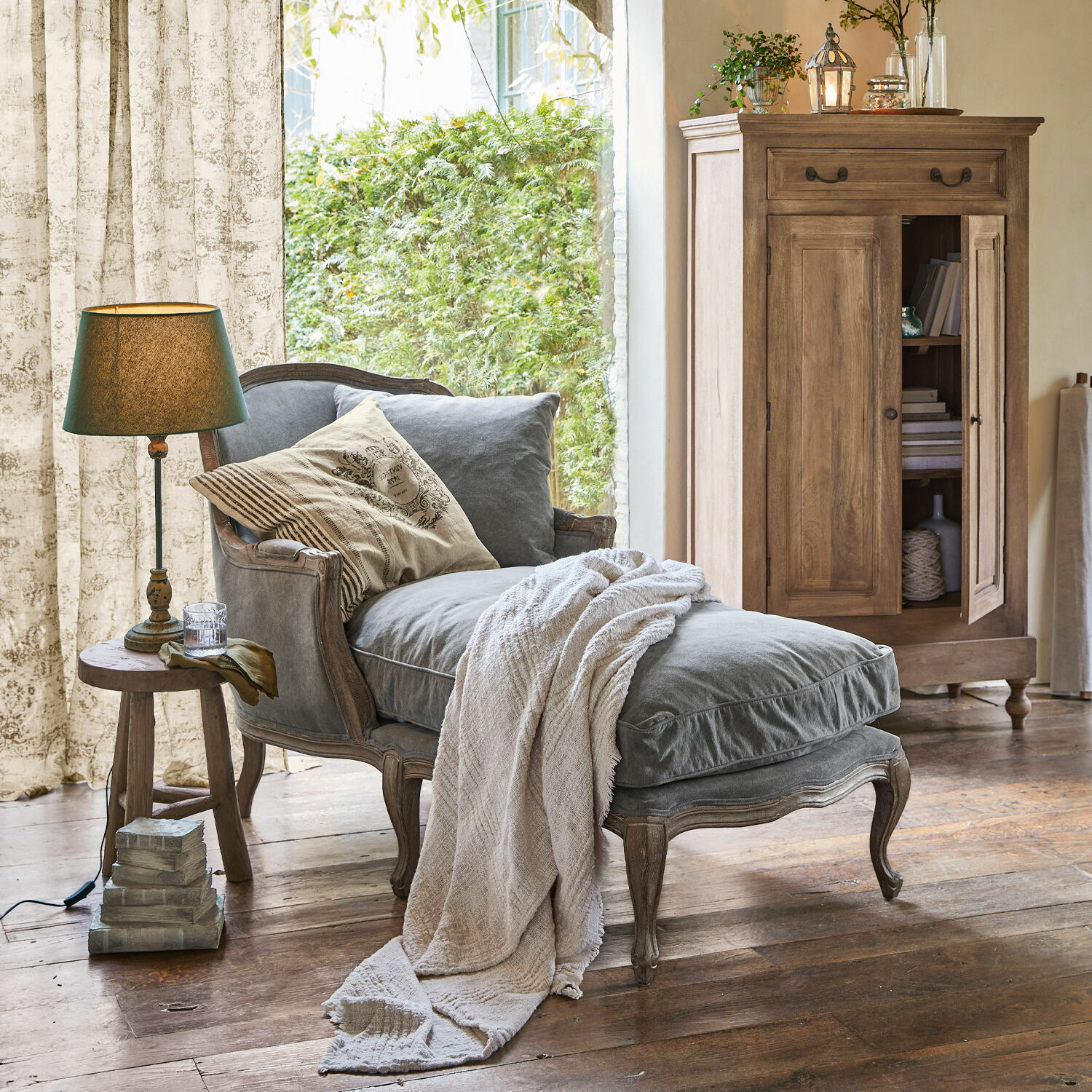 Méridienne Muel Chaise longue grise en tissu avec cadre en bois et couverture beige dans un salon rustique