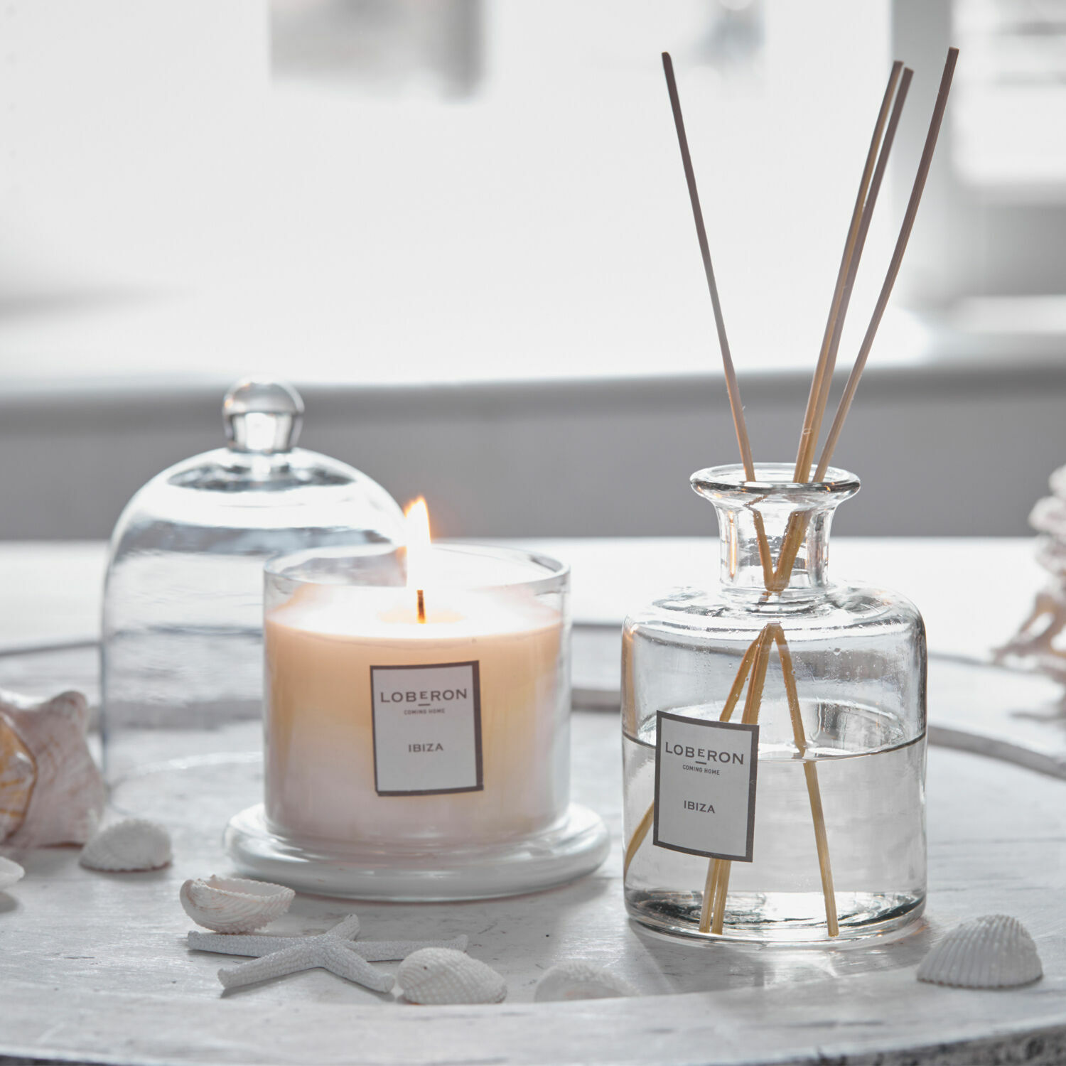 Coffret de senteurs Vanis Bougie parfumée et diffuseur en verre transparent avec bâtonnets sur un plateau blanc décoré de coquillages