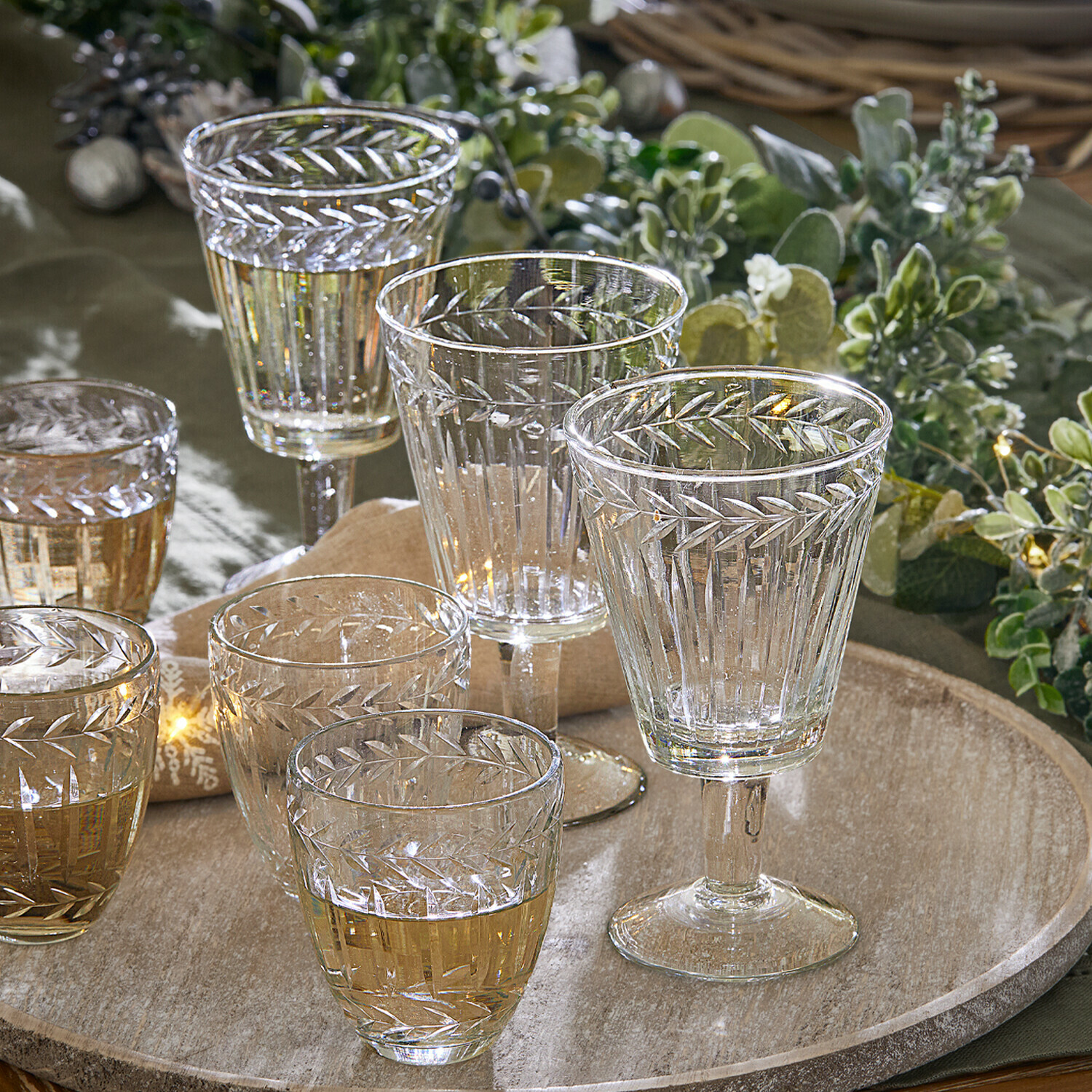 Lot de 12 verres Padiès Ensemble de verres et coupes en verre transparent avec motif gravé de feuilles sur un plateau en bois