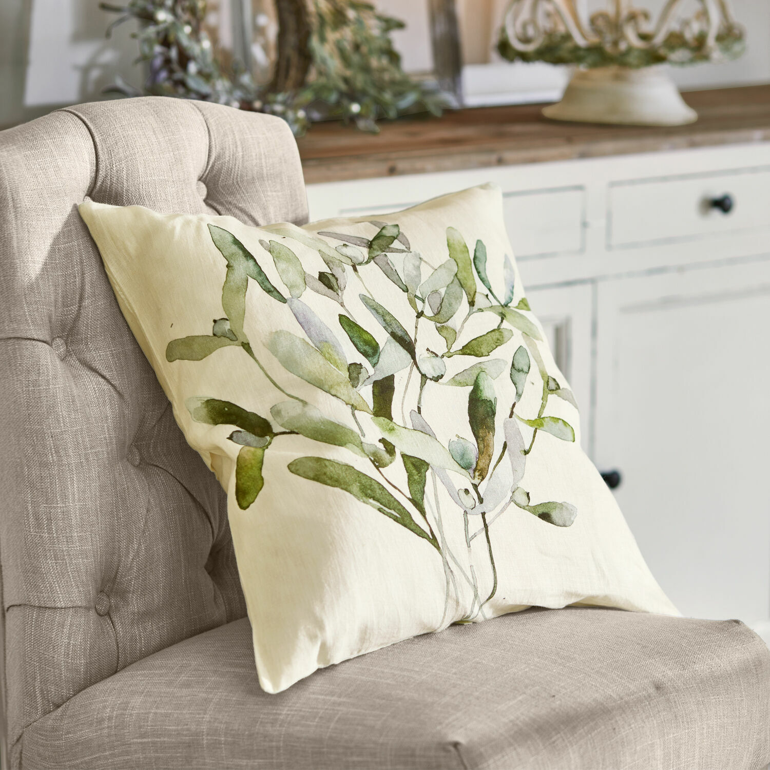 Housse de coussin Mistletoe Coussin beige avec motif de feuilles vertes sur fauteuil gris dans un intérieur naturel