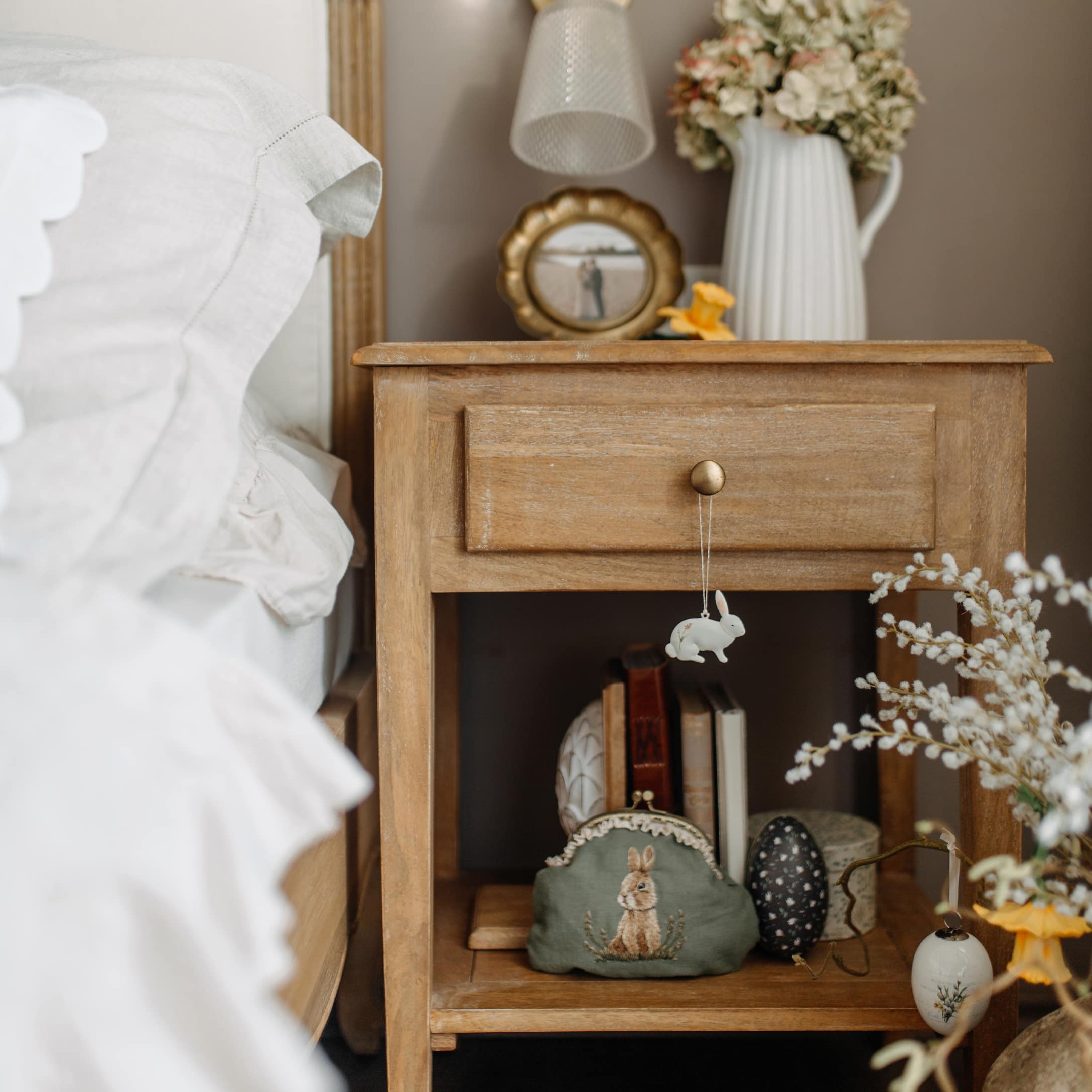 Table de chevet en bois avec décorations de Pâques et pochette verte brodée d'un lapin dans une chambre