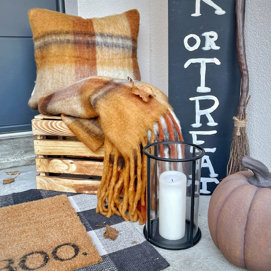 Plaid et coussin orange et marron doux avec franges sur caisse en bois à l'entrée