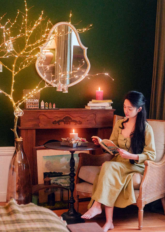 Femme lisant un livre dans un salon chaleureux avec mur vert, bougies et table décorative noire