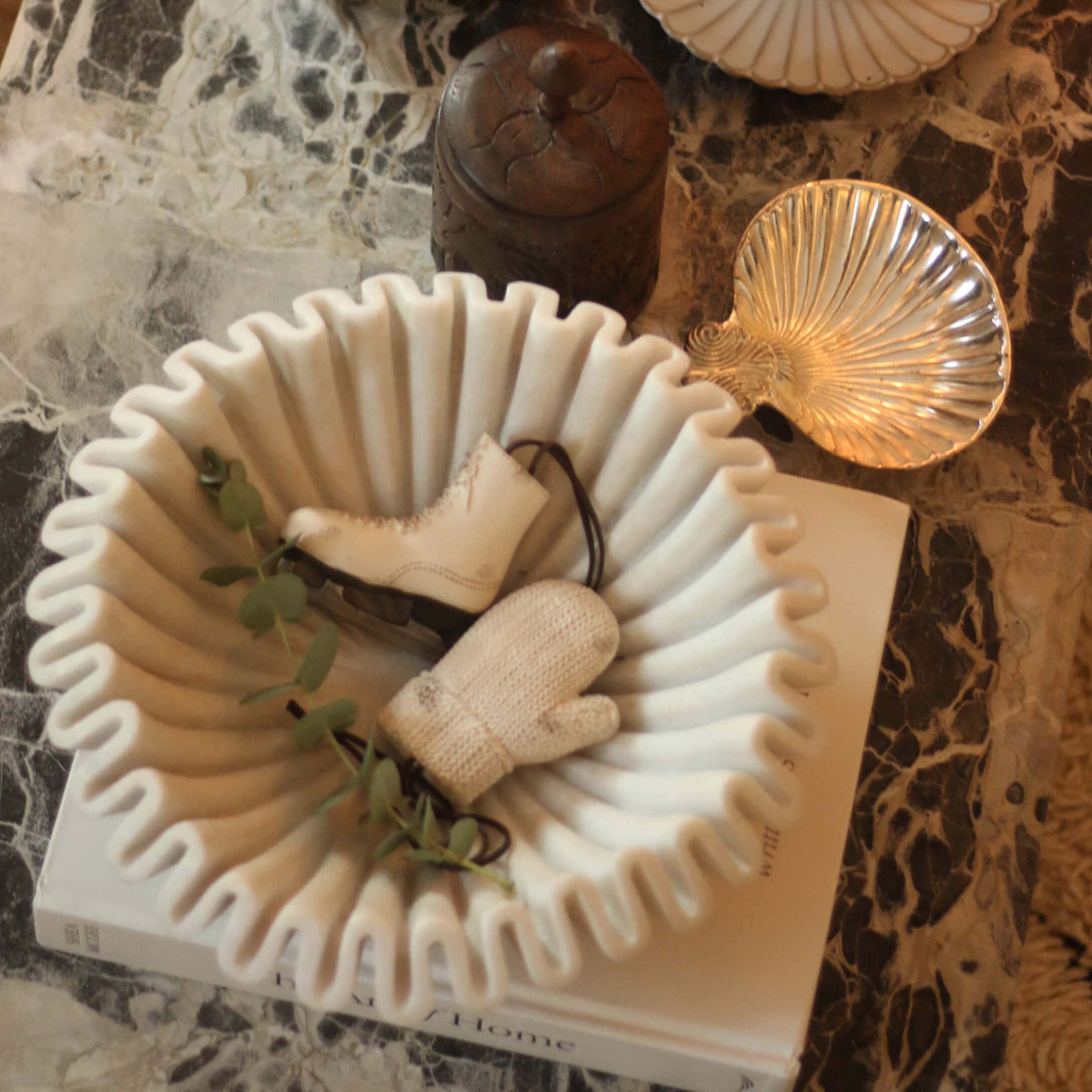 Bol en céramique blanche à bords ondulés avec décorations patin et moufle sur table en marbre