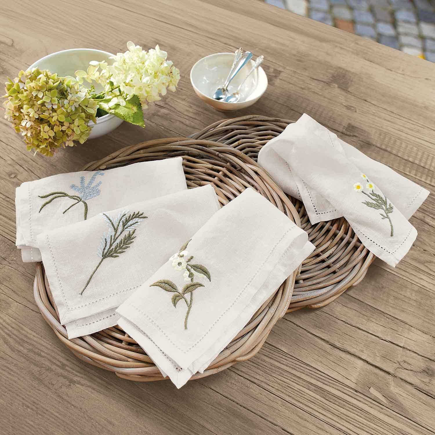 Serviettes en lin crème avec broderies florales posées sur un plateau en osier sur une table en bois