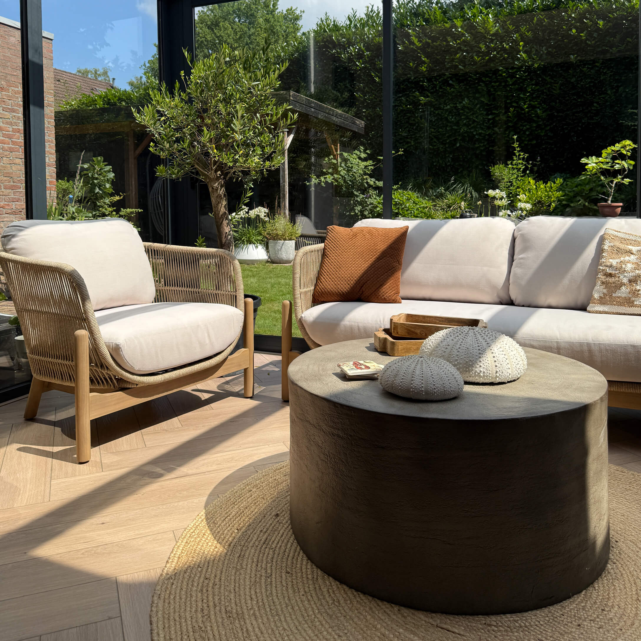 Salon moderne avec canapé beige, fauteuil en bois et tissu, table basse ronde noire et décorations naturelles