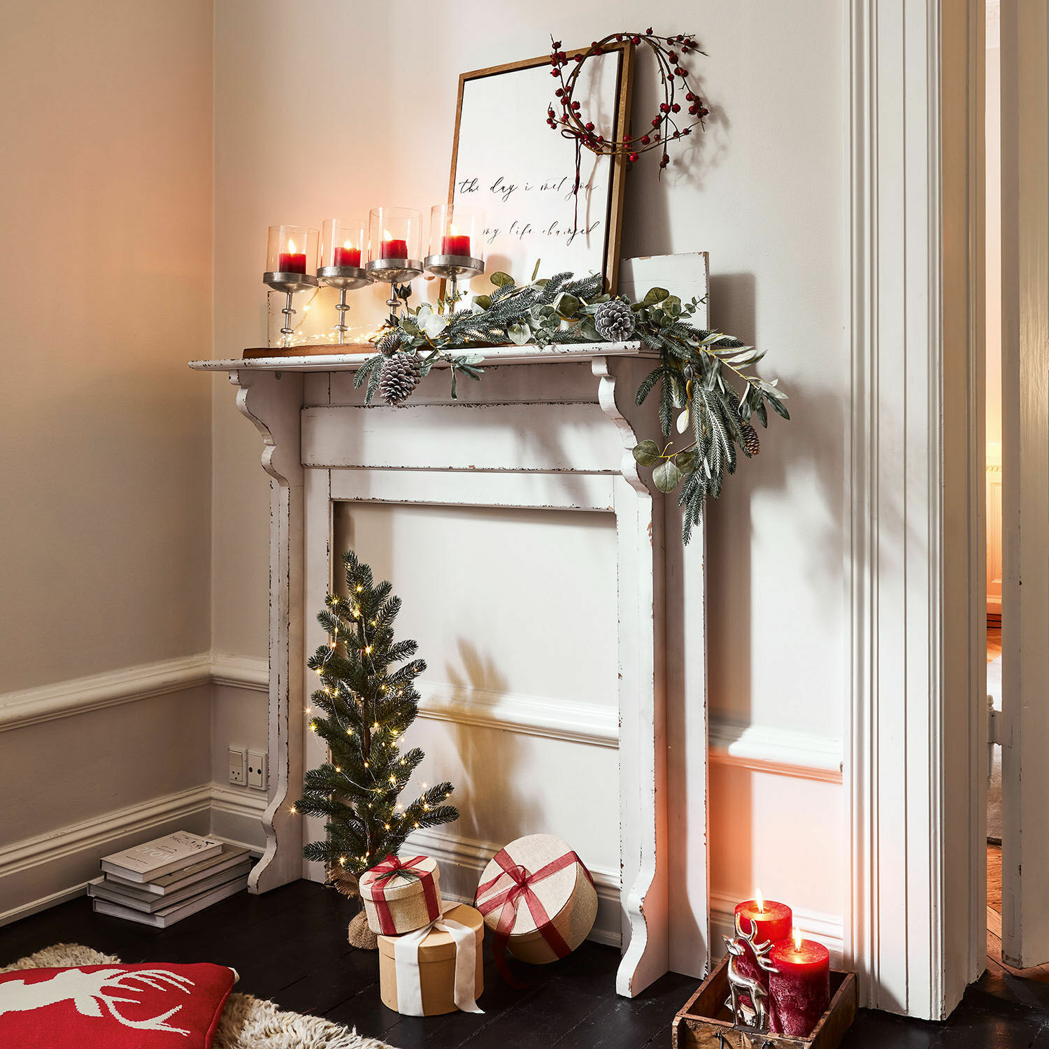 Manteau de cheminée Cessieu Cheminée décorative blanche en bois avec guirlande verte, bougies rouges et cadeaux de Noël