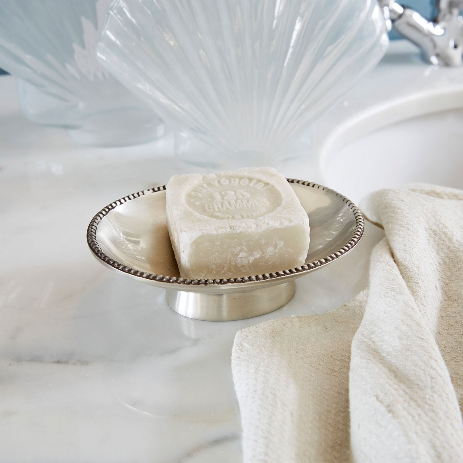 Savon blanc carré sur porte-savon en argent à côté d'une serviette crème sur un comptoir en marbre