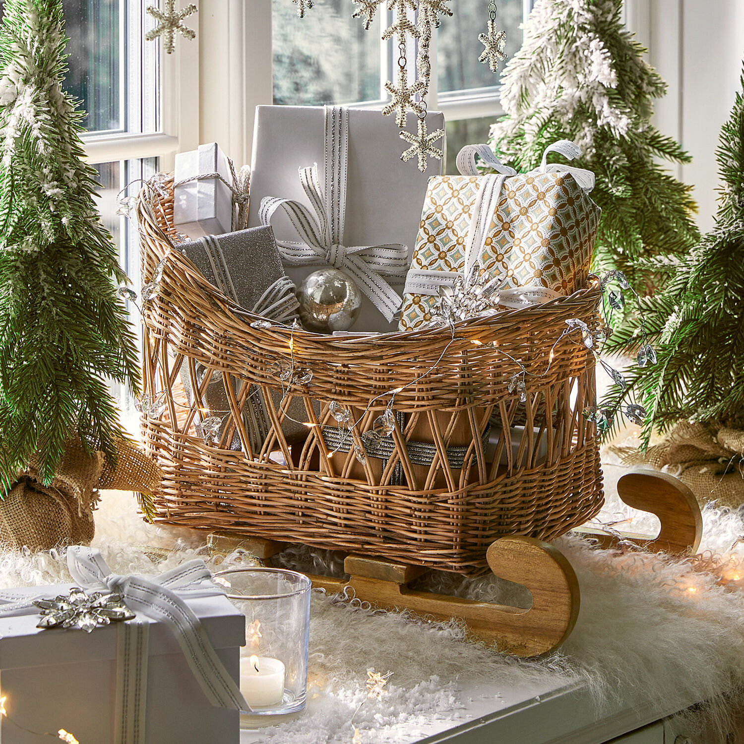 Traineau décoratif Quileta Luge en osier avec patins en bois remplie de cadeaux emballés en blanc et argent dans un décor de Noël