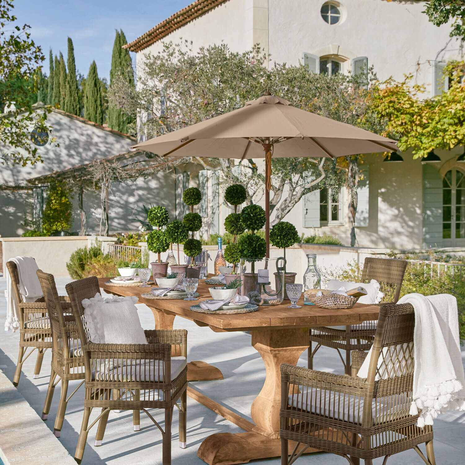 Parasol Brent Grande table de jardin en bois avec chaises en osier et parasol beige sur terrasse ensoleillée