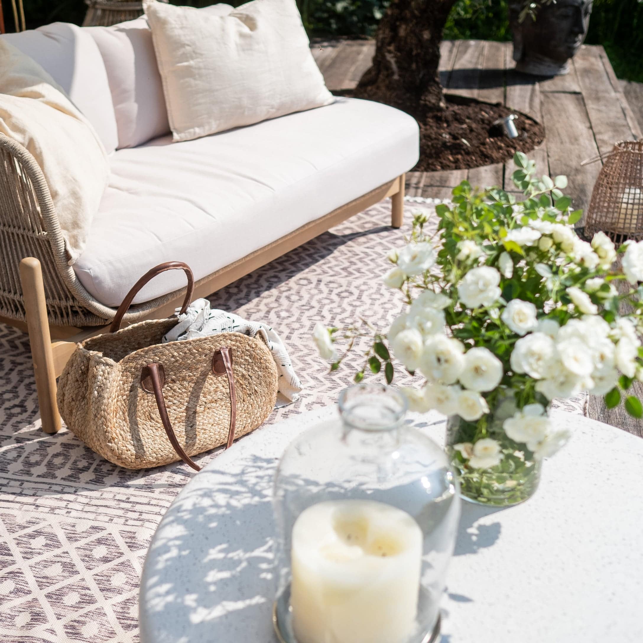 Fauteuil blanc confortable avec coussins en extérieur, sac en osier et fleurs blanches fraîches sur la table