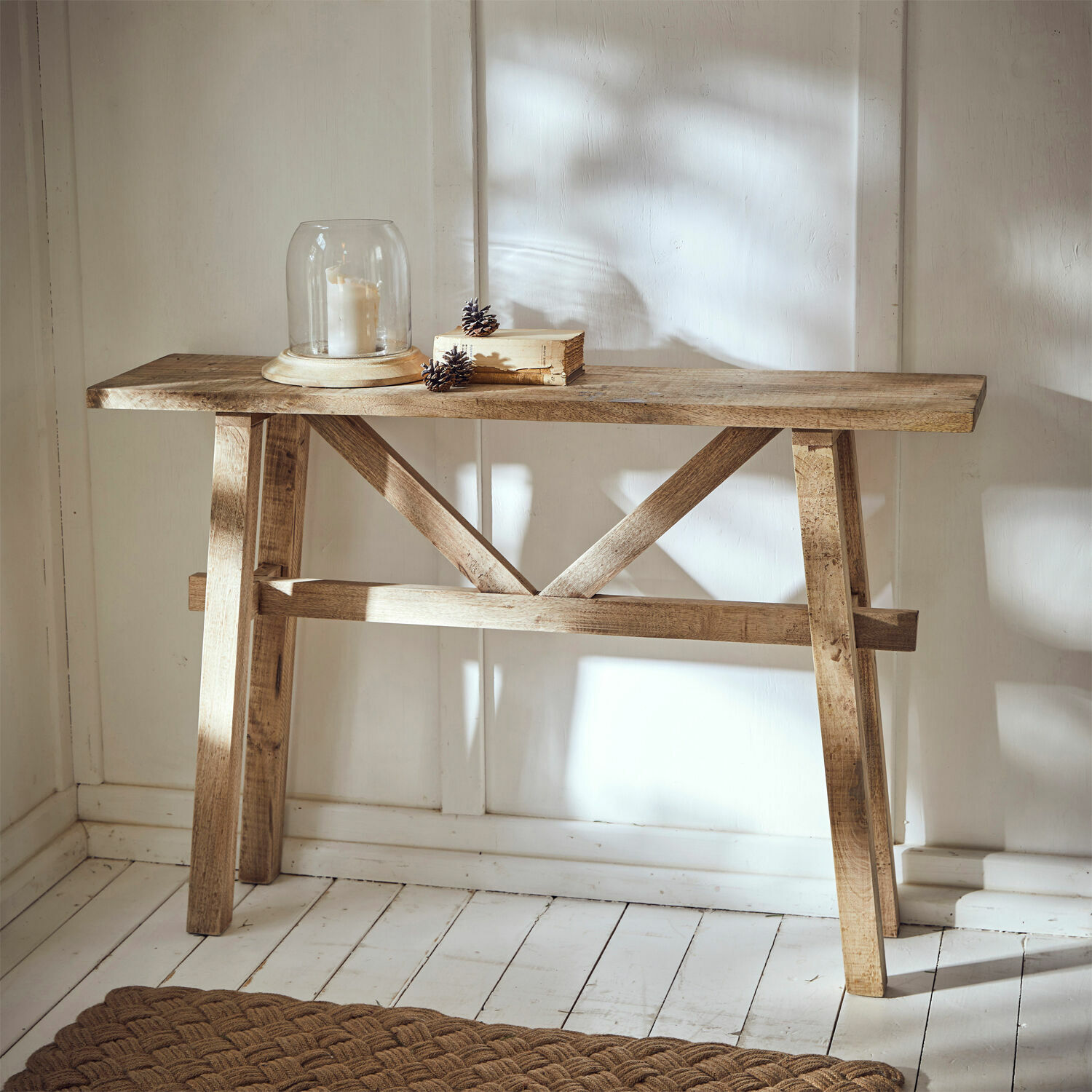 Console Nael Table console en bois naturel avec bougie sous cloche et livre sur un sol blanc en bois