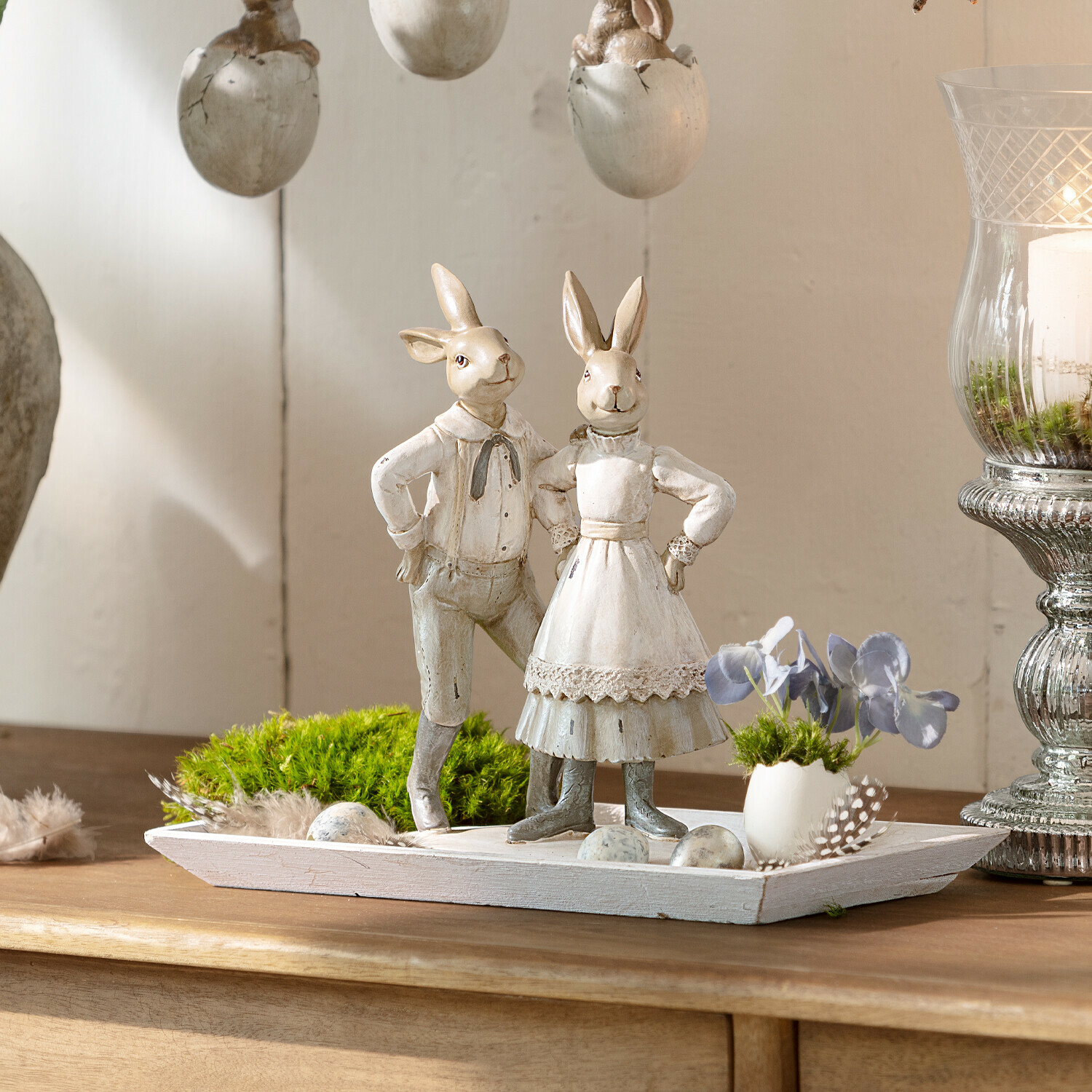 Lapins Paire Décoration avec deux lapins en bois vêtus de blanc sur un plateau en bois avec mousse verte et œufs décoratifs
