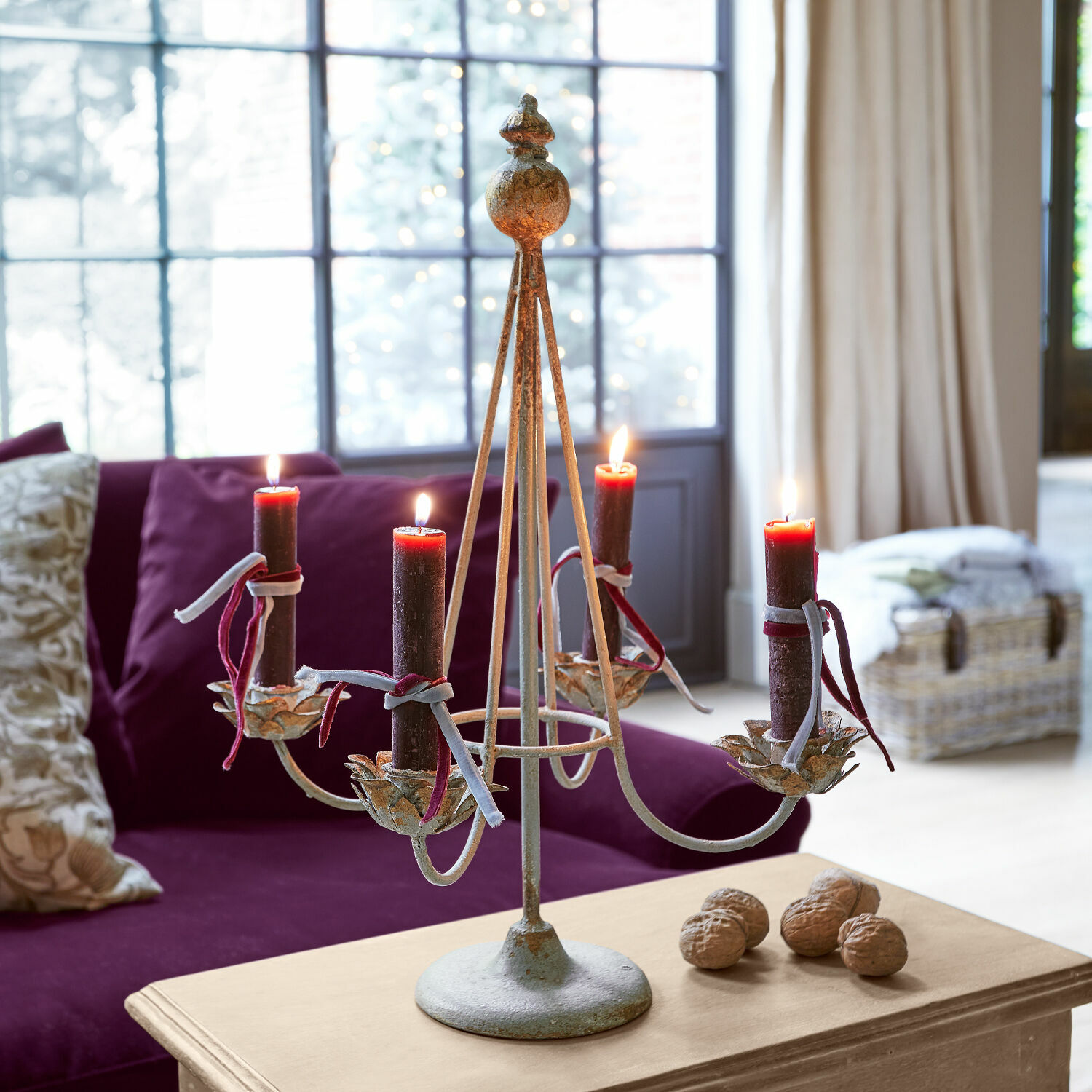 Bougeoir porte-couronne Liyanah Chandelier en métal avec quatre bougies rouges sur une table en bois dans un salon avec canapé violet
