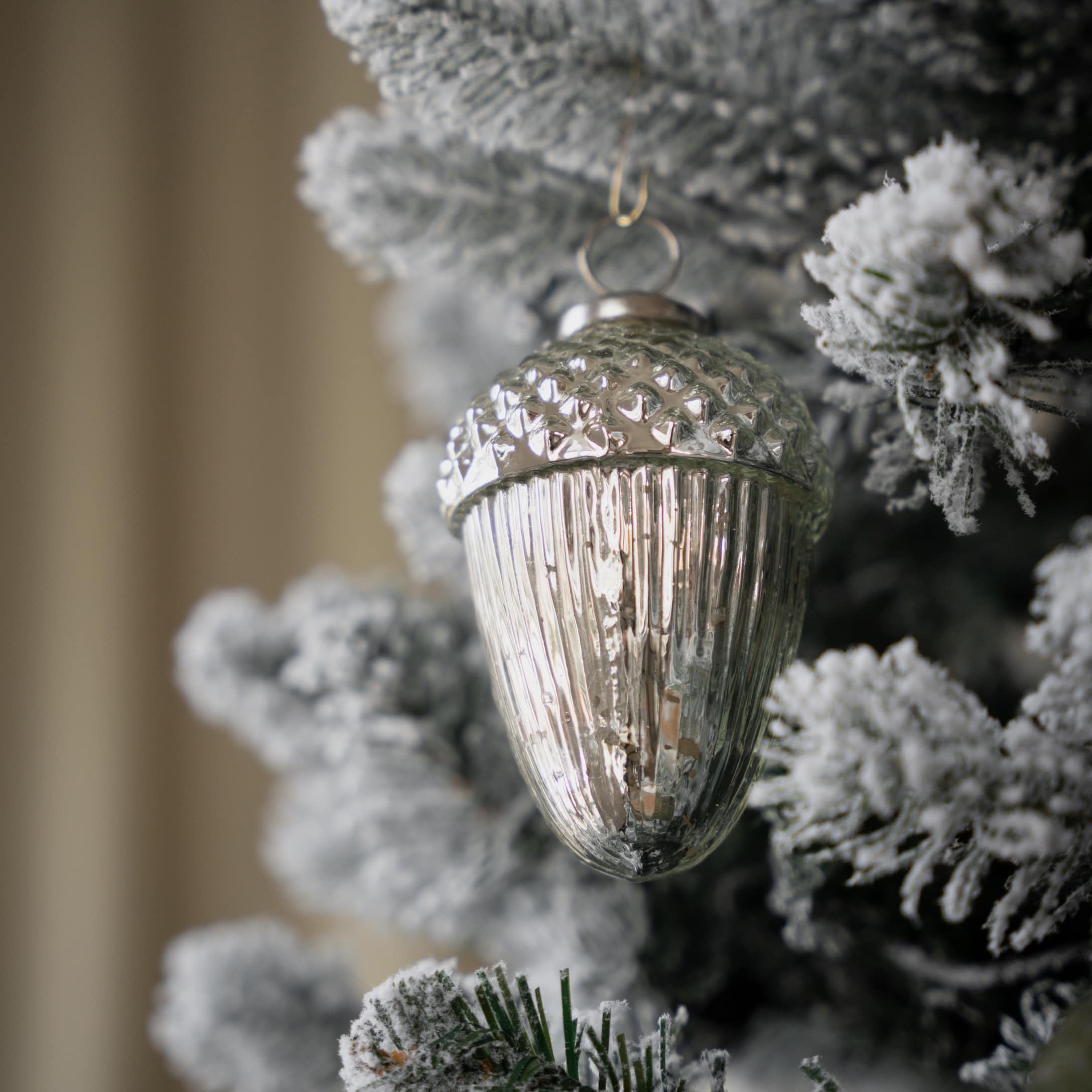 Décoration de Noël en forme de gland en verre argenté sur sapin enneigé blanc