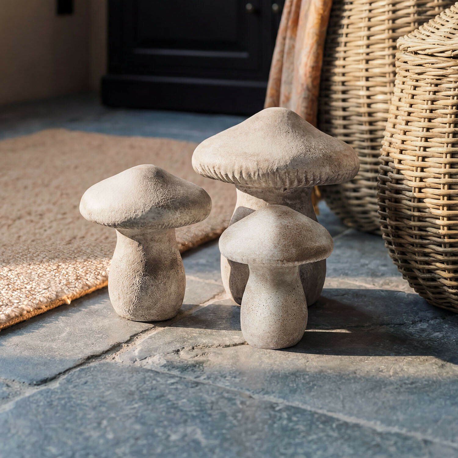 Lot de 3 champignons Rynmor Trois champignons décoratifs en béton couleur naturelle posés sur un sol en pierre dans un style rustique