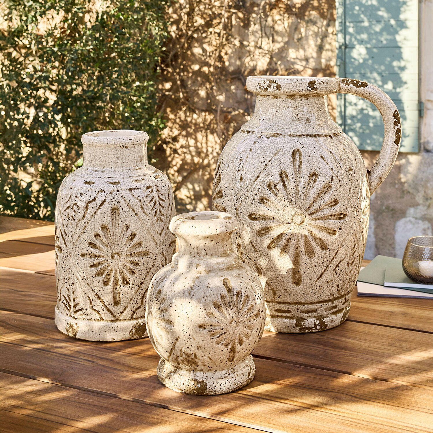 Ensemble de trois vases en céramique crème avec motifs bruns posés sur une table en bois en extérieur