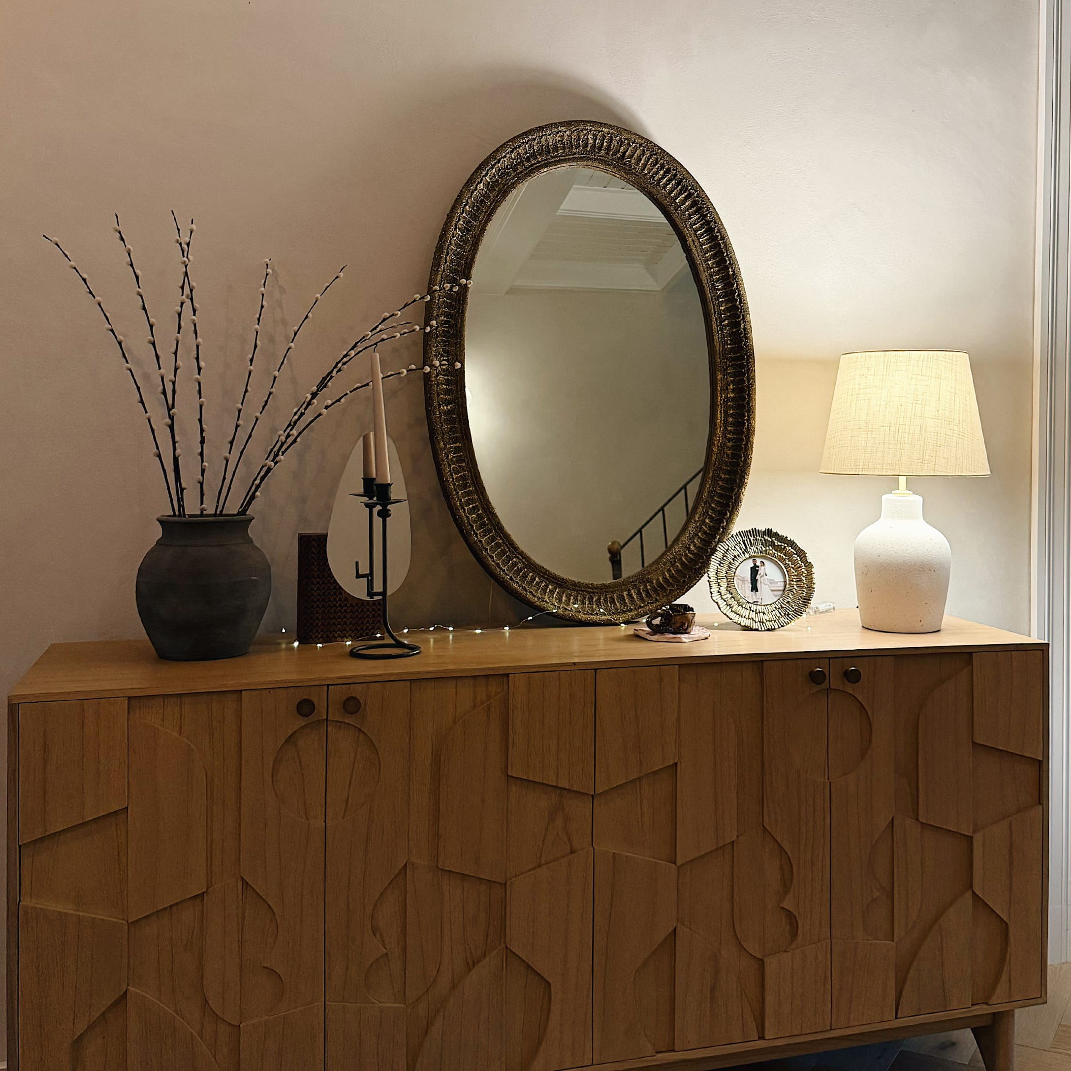 Buffet en bois avec motif géométrique, miroir ovale, lampe blanche et vase avec branches décoratives