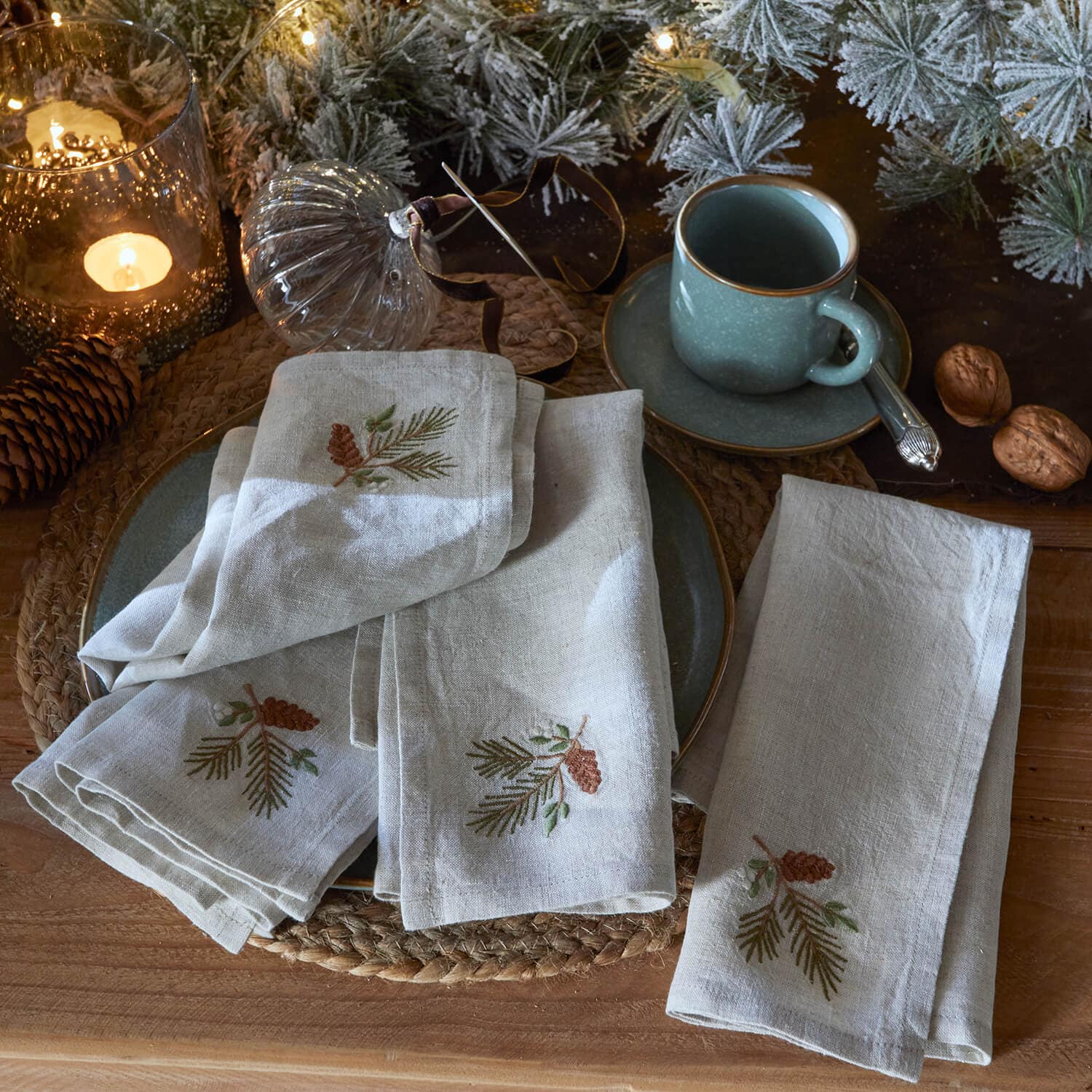Serviettes en lin brodées de pommes de pin sur table rustique avec tasse verte et décorations de Noël