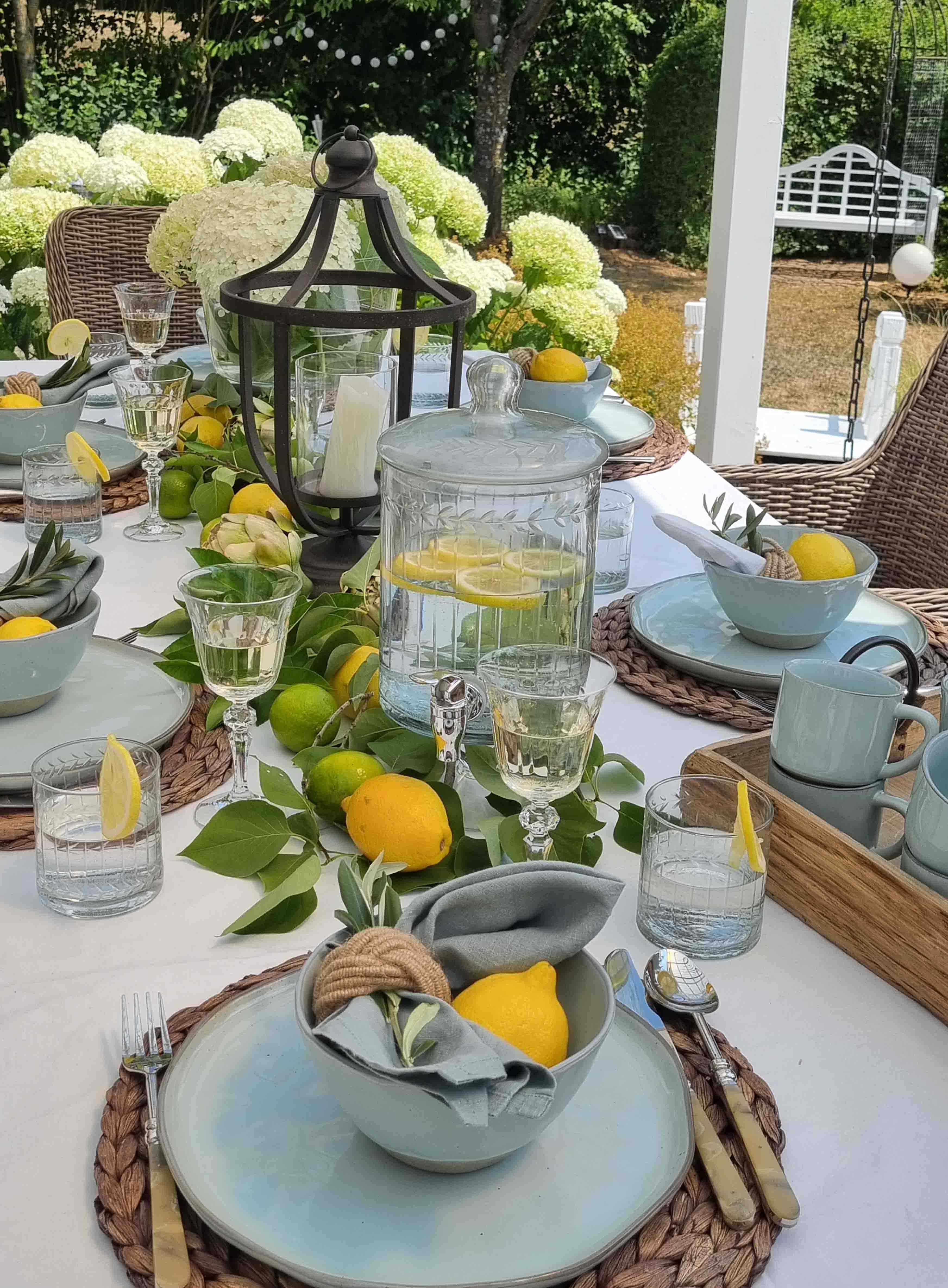 Table d'été en céramique bleue avec citrons et lanterne, décorée de fleurs blanches en arrière-plan