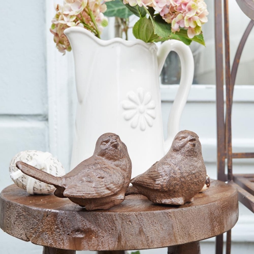 Oiseaux décoratifs en fonte marron posés sur une table en bois avec un pichet blanc en arrière-plan