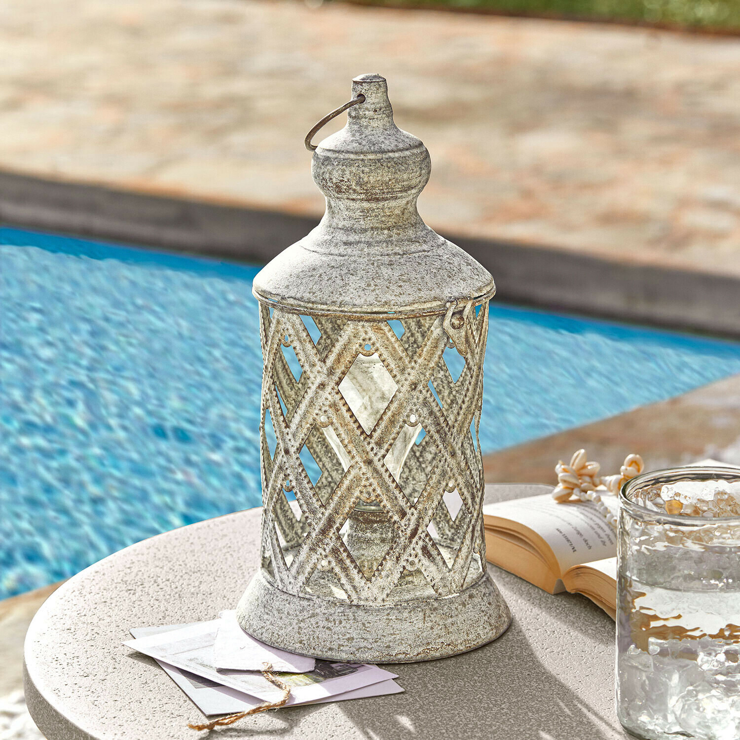 Lanterne LED Lavorie Lanterne décorative en métal argenté vieilli sur une table près de la piscine avec livre et verre d'eau