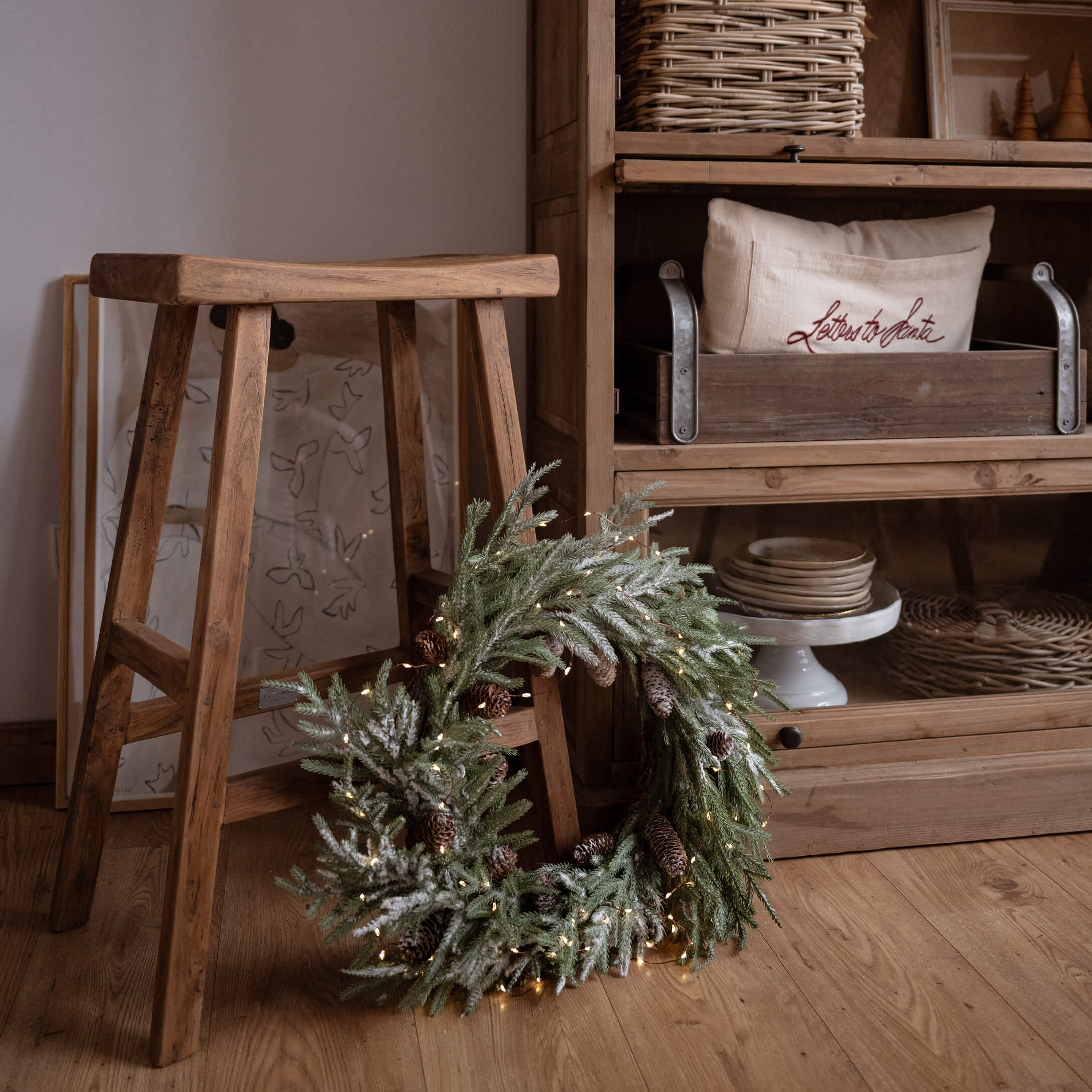 Couronne de Noël décorative avec branches vertes et pommes de pin posée sur un sol en bois près d'un tabouret