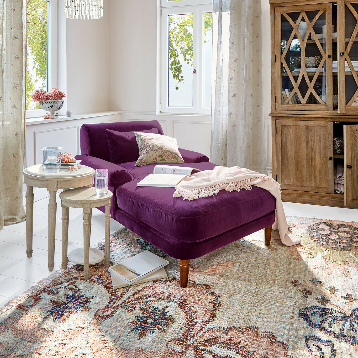 Chaise longue en velours violet dans un salon lumineux avec buffet en bois et tables rondes