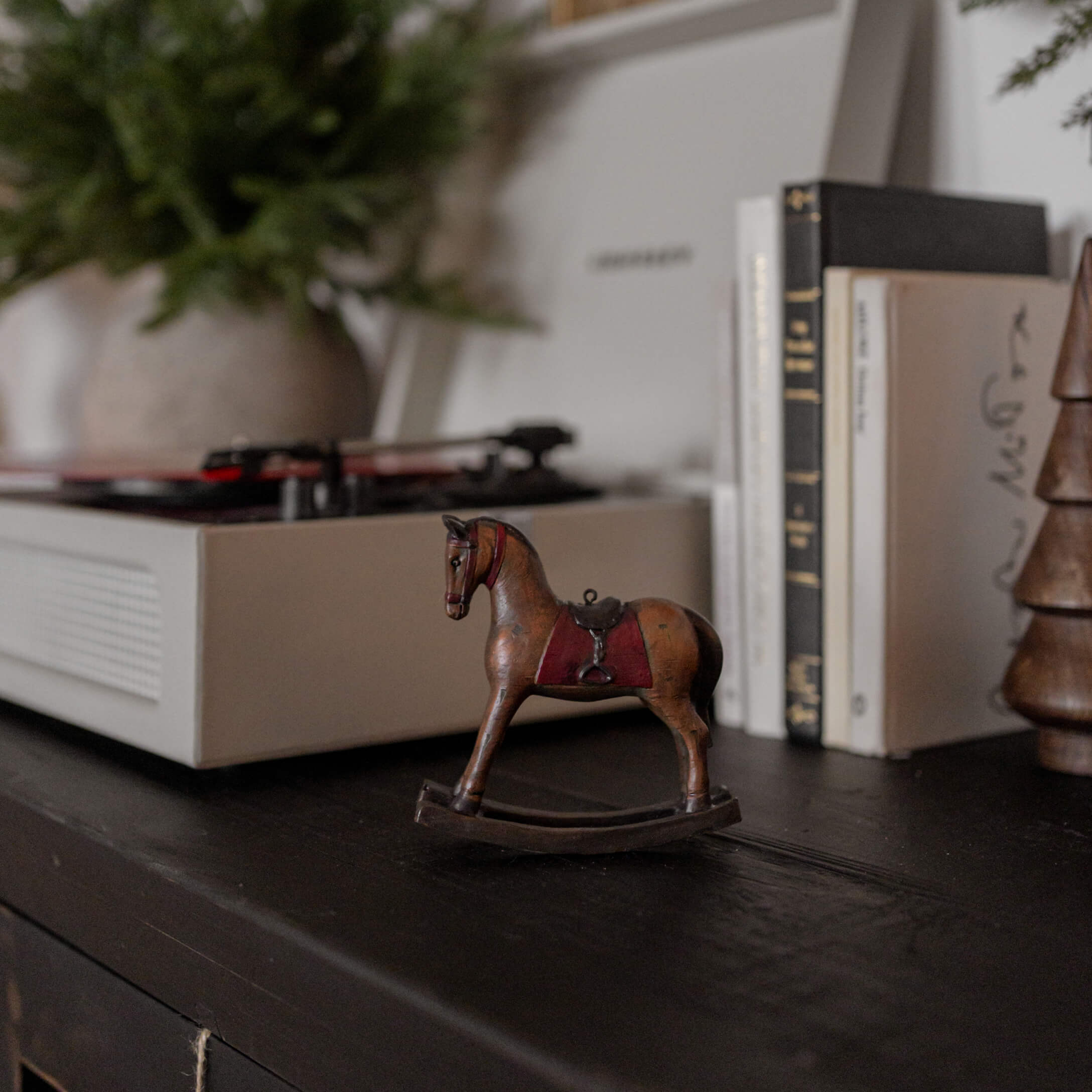 Cheval à bascule en bois marron avec selle rouge sur surface noire près de livres et platine vinyle
