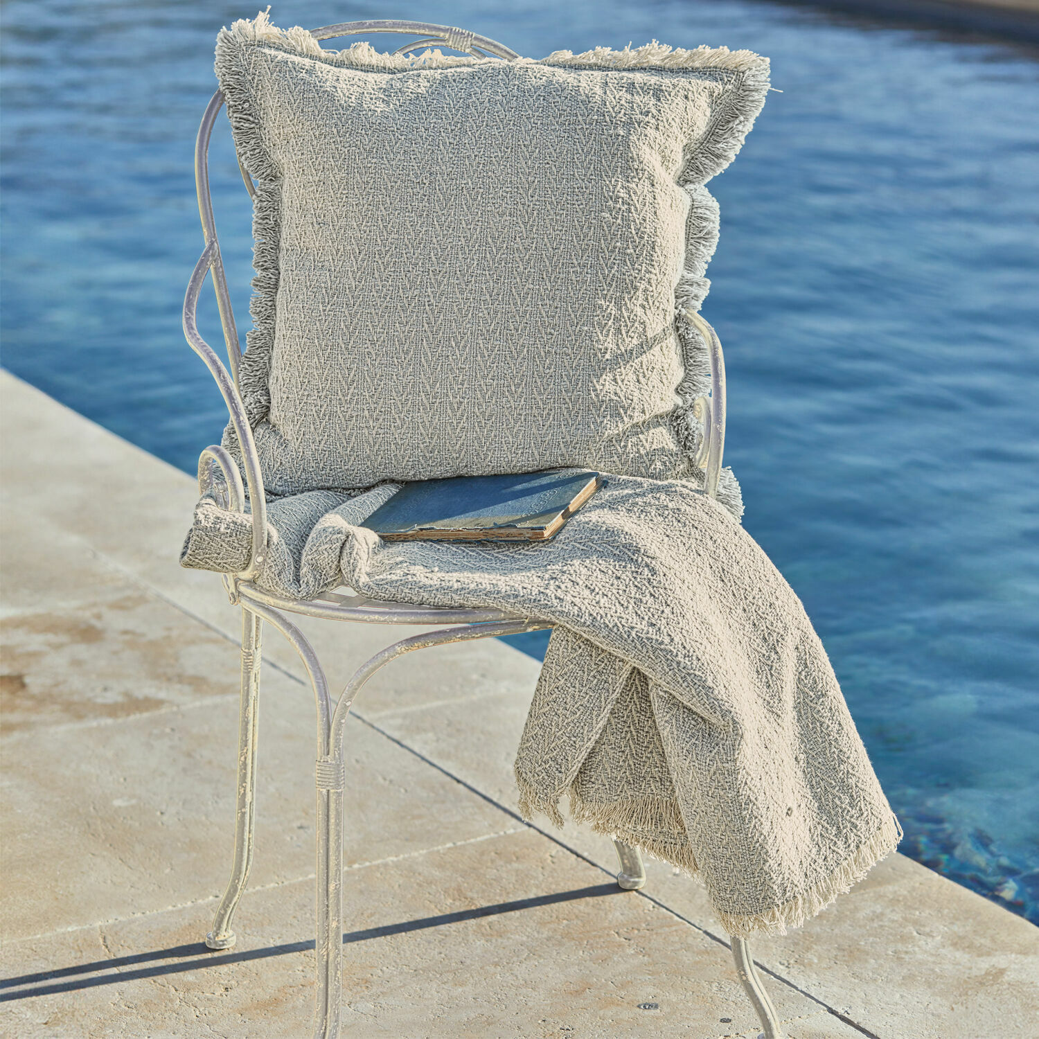 Chaise Aube Coussin beige et plaid à franges sur chaise en métal au bord de l'eau, décoration intérieure et extérieure