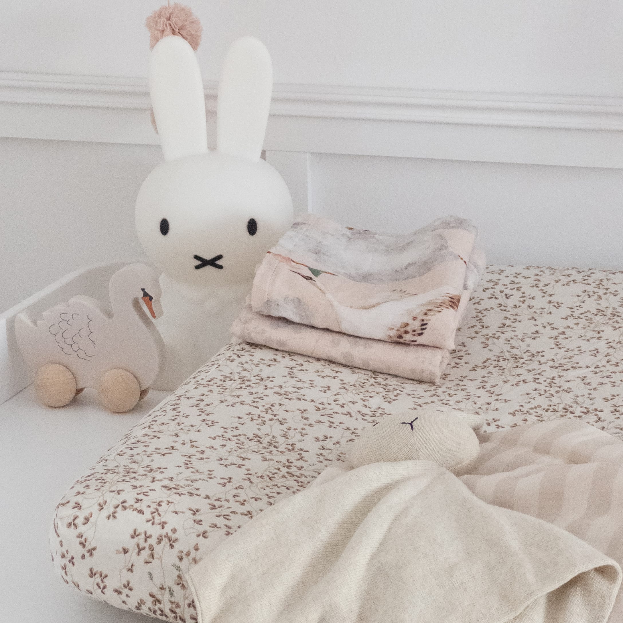 Lit bébé avec drap beige à motif floral et jouet en bois cygne dans une chambre claire