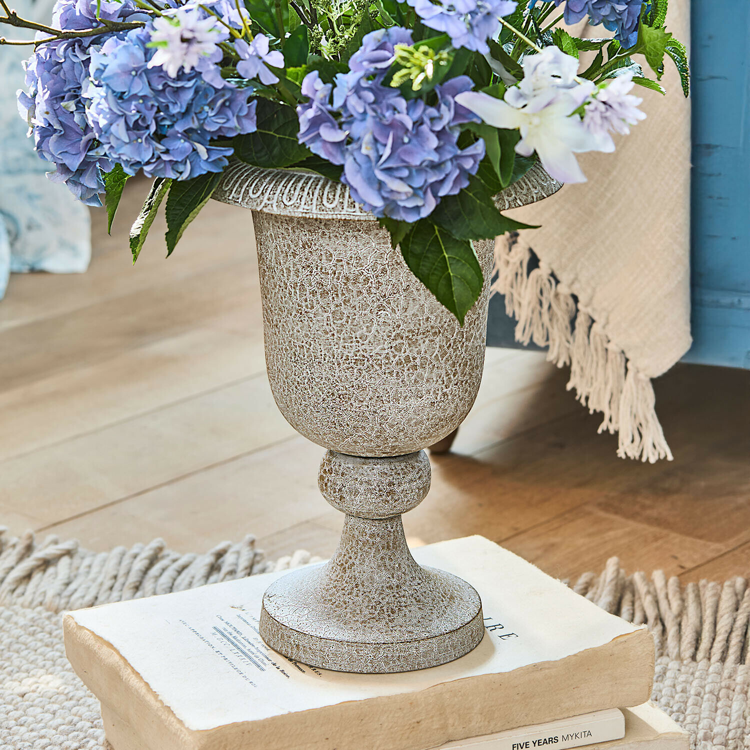 Vase Vittoriane Vase décoratif en céramique vieillie beige avec fleurs bleues posé sur des livres anciens