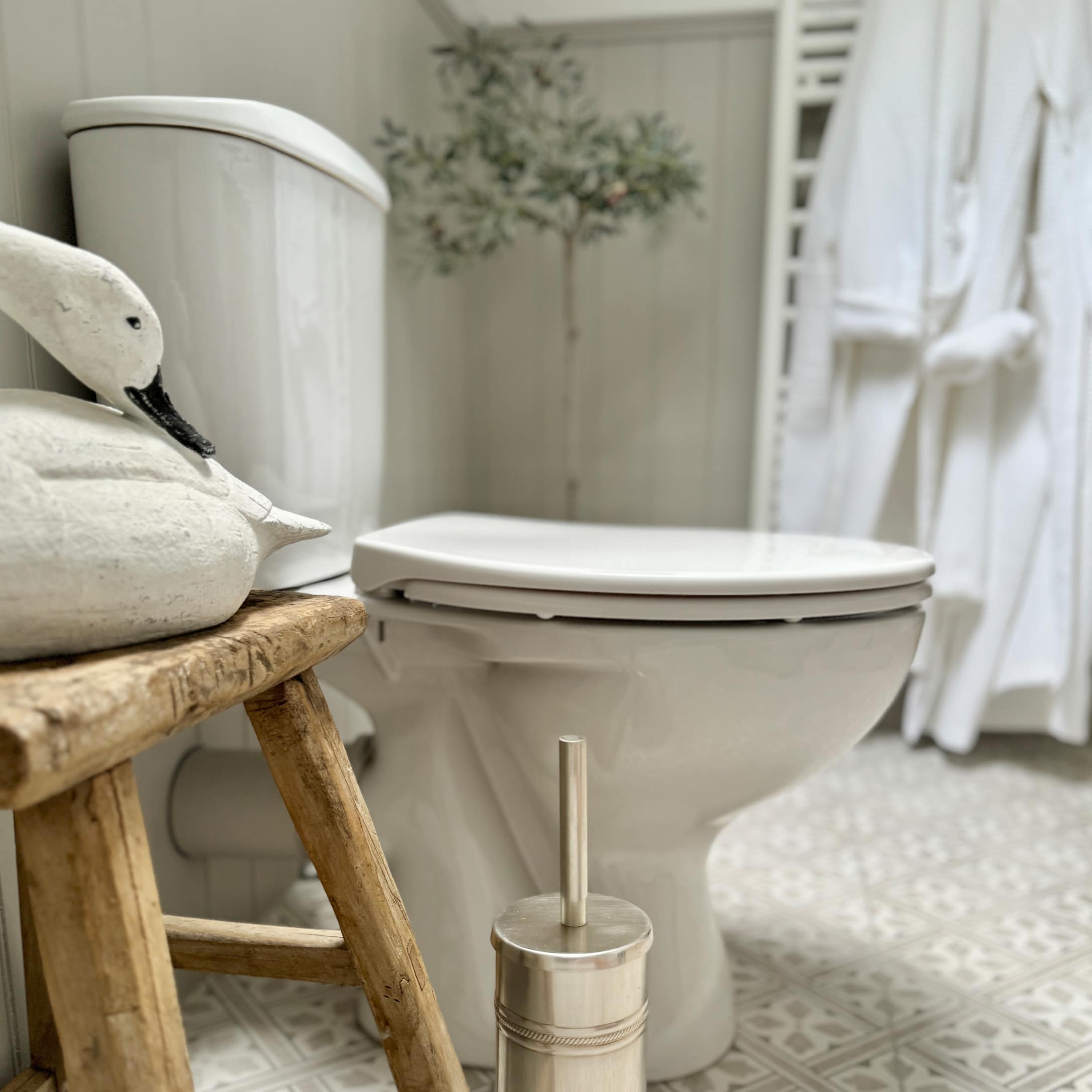 Toilettes en céramique blanche dans une salle de bain avec tabouret en bois et brosse WC métallique