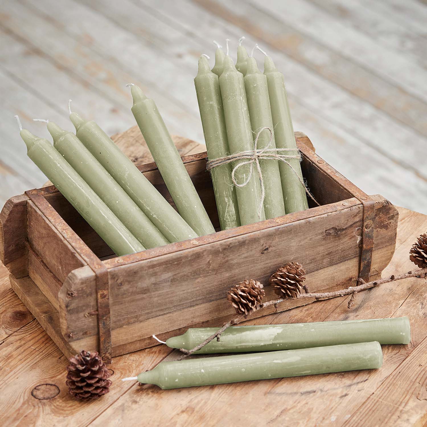 Lot de bougies vertes en cire dans une boîte en bois sur une table rustique avec des pommes de pin