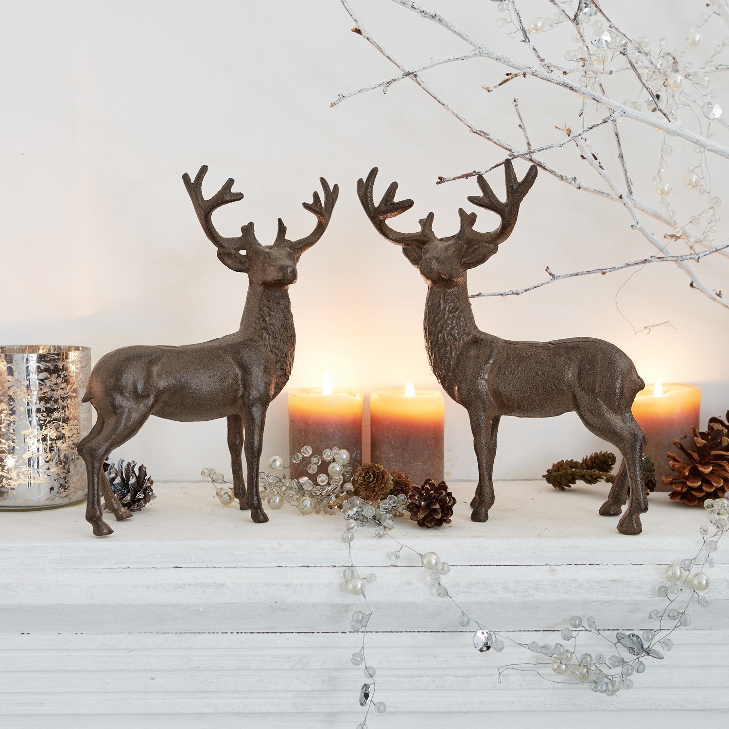 Lot de 2 cerfs décoratifs Friends Deux décorations de cerfs en métal brun sur une étagère blanche avec bougies et pommes de pin