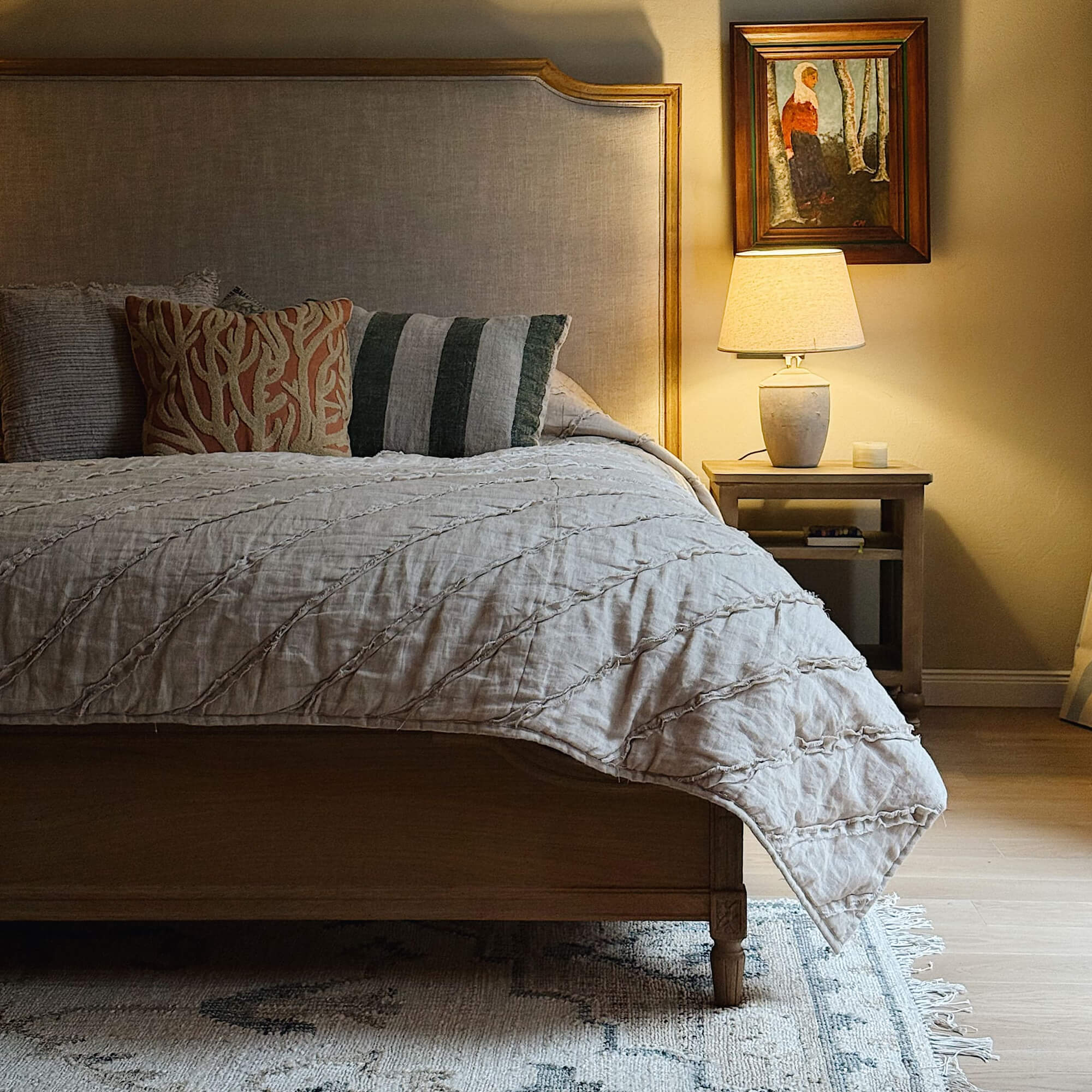 Lit en bois avec tête de lit beige rembourrée dans une chambre chaleureuse avec lampe et tableau