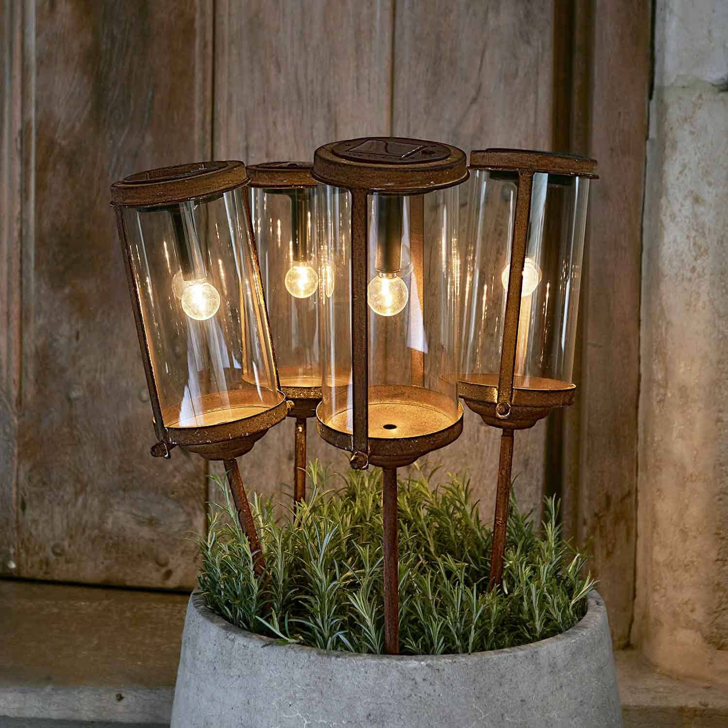 Ensemble de quatre lampes de jardin rouillées avec abat-jours en verre et supports métalliques dans un pot