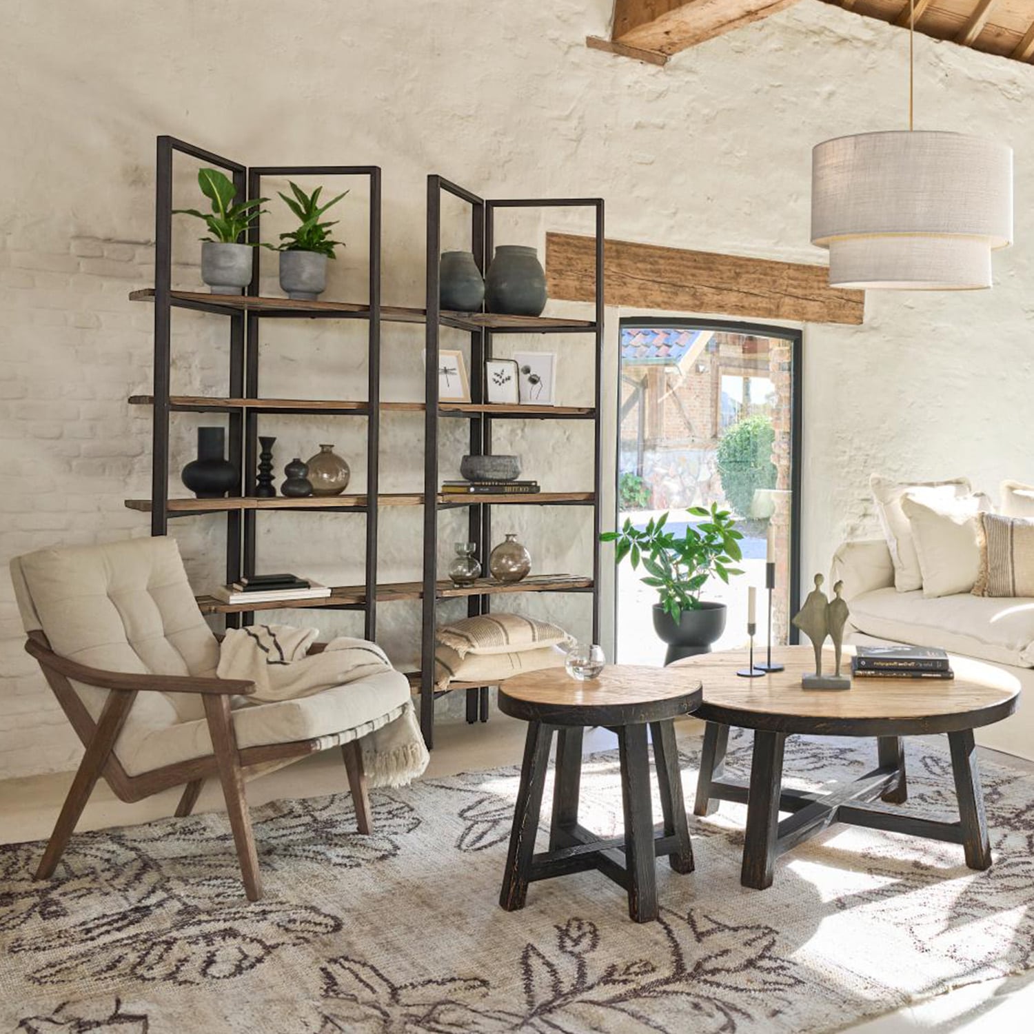 Salon chaleureux avec fauteuil en bois, étagère métal et bois, tables basses rondes sur tapis à motifs