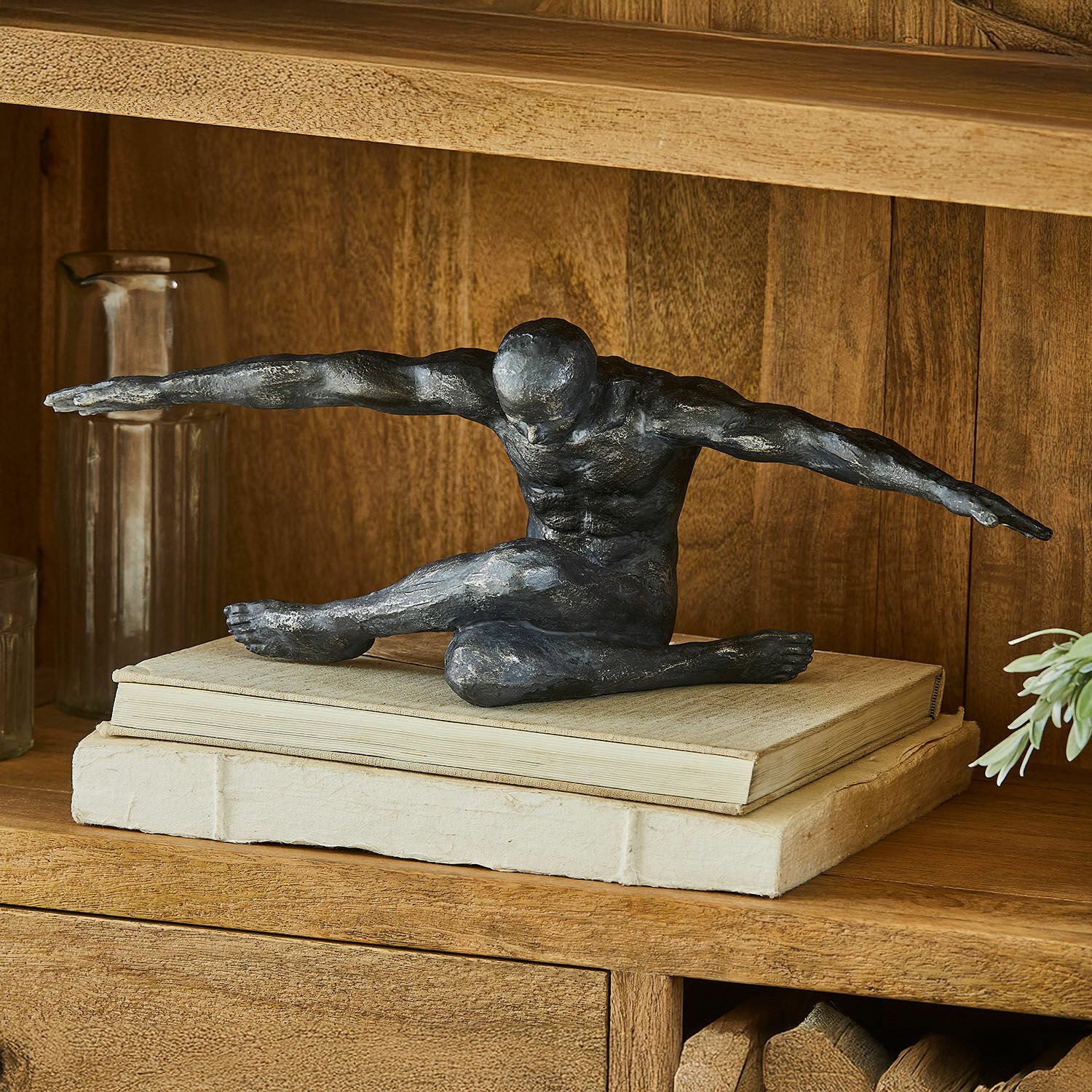 Statuette Smitty Sculpture noire d'une figure masculine aux bras étendus posée sur des livres sur une étagère en bois décorative