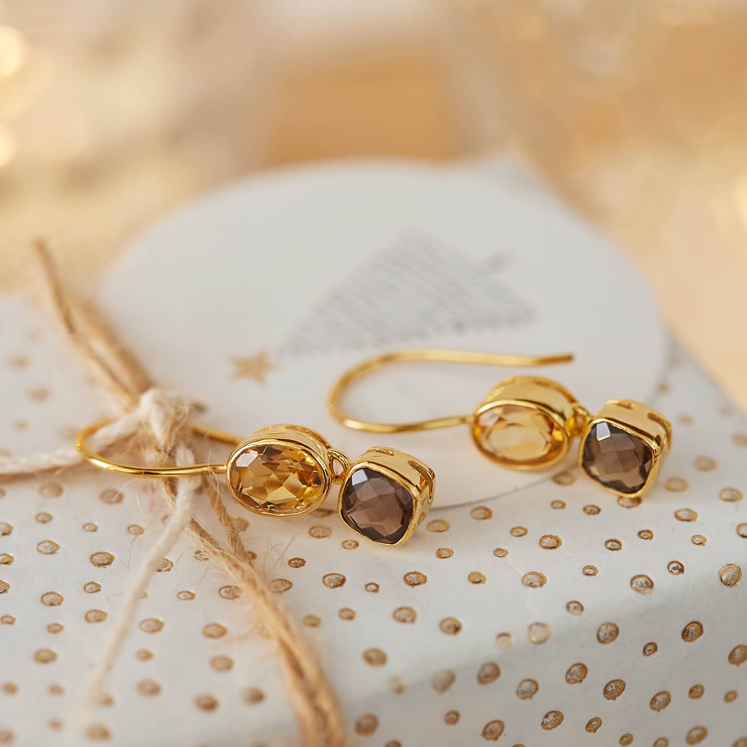 Boucles d'oreilles dorées avec pierres facettées marron et ambre sur fond décoratif festif