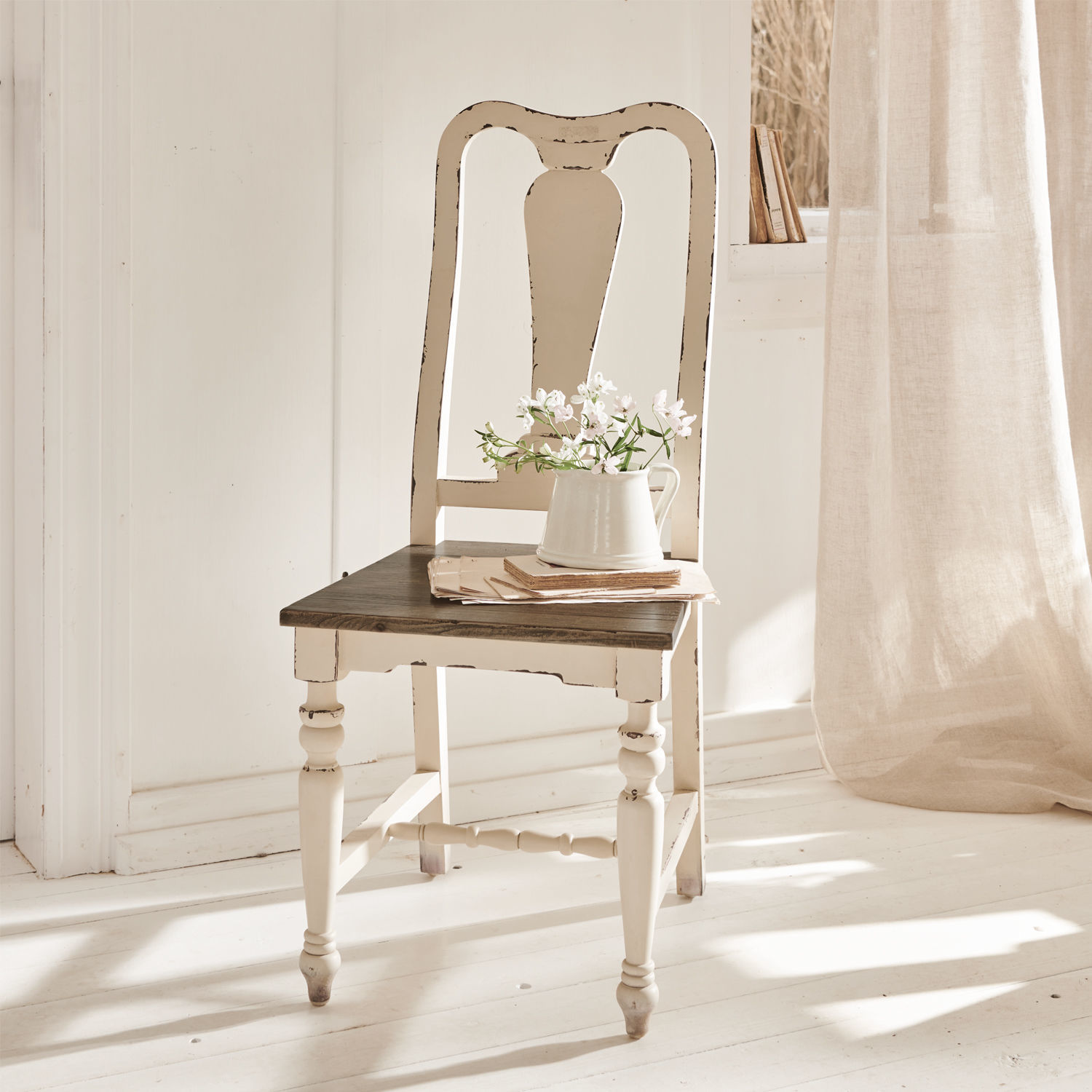 Chaise Harry Chaise vintage en bois blanc avec assise foncée et pichet à fleurs dans une pièce lumineuse