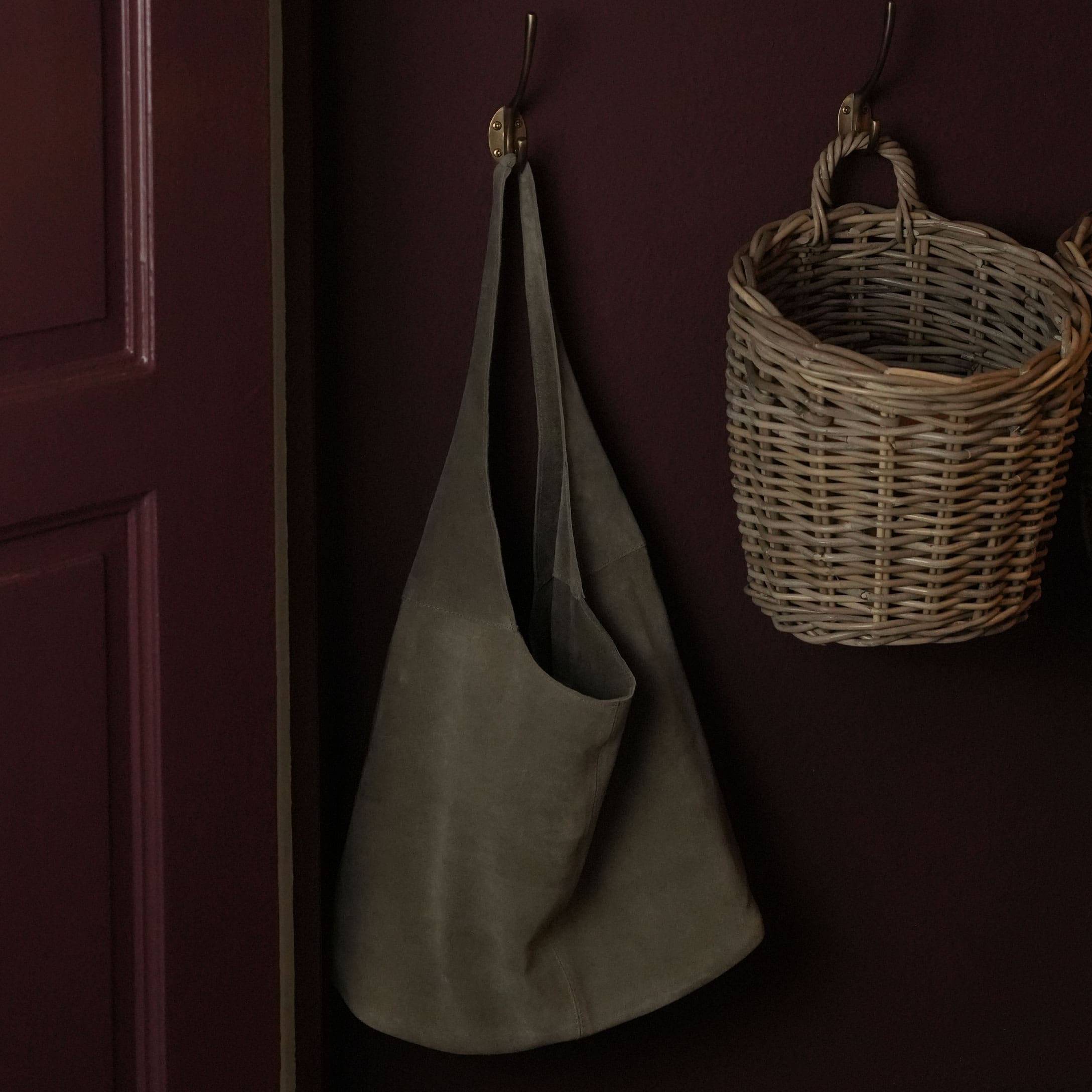 Tablier en daim gris suspendu à un crochet en cuivre à côté d'un panier en osier sur un mur sombre