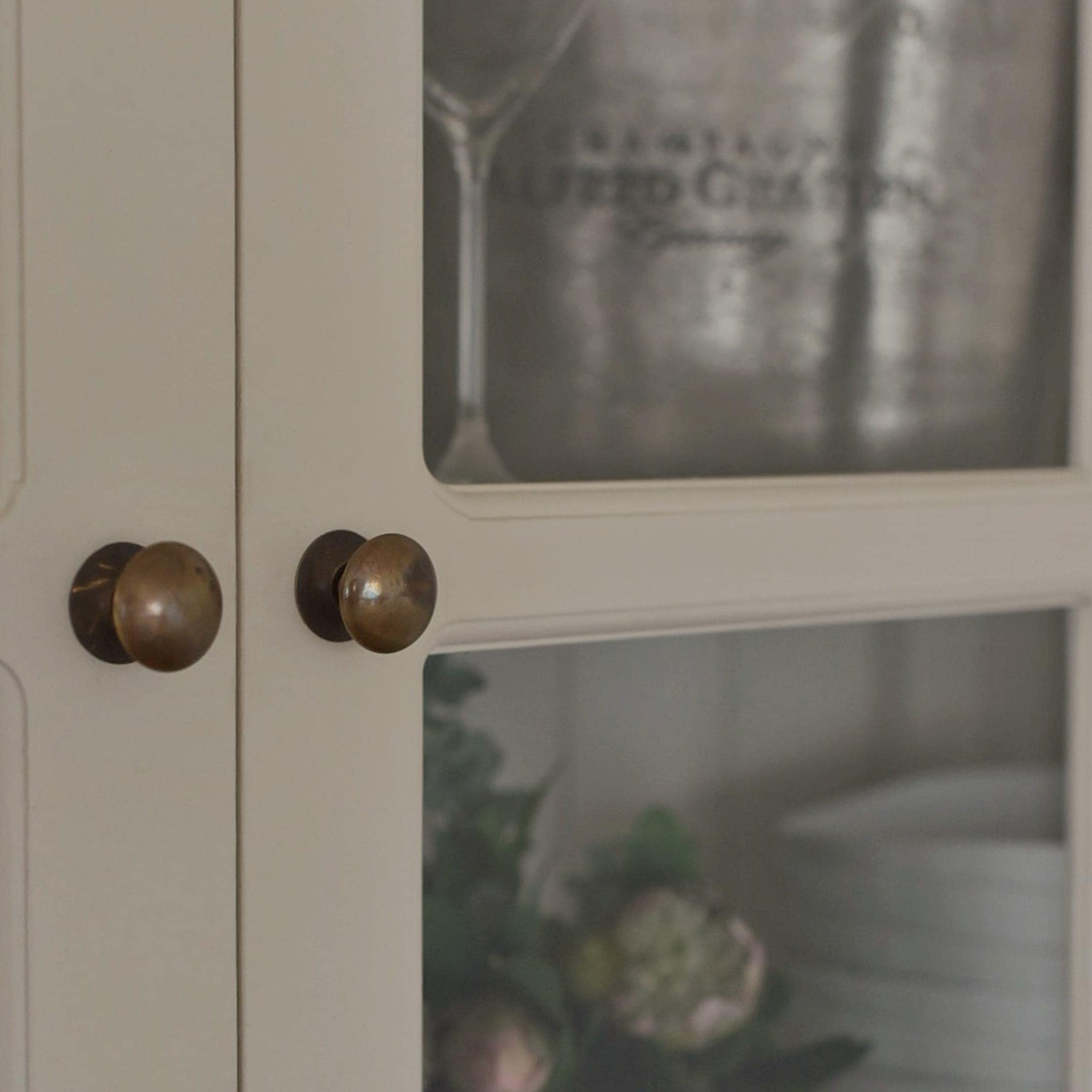 Détail d'une armoire blanche en bois avec poignées en laiton et portes vitrées pour vaisselle