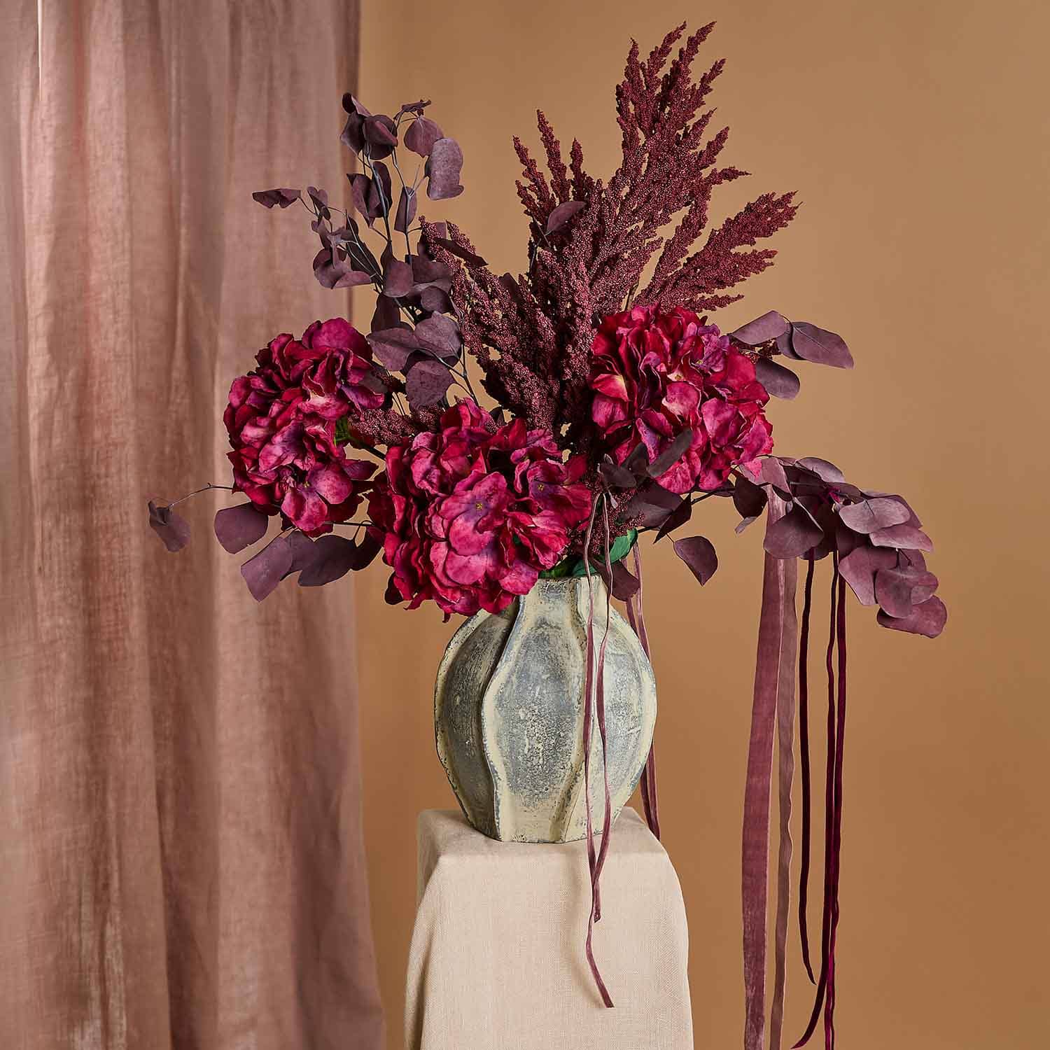 Bouquet de fleurs artificielles bordeaux dans un vase en céramique sur fond beige, décoration intérieure