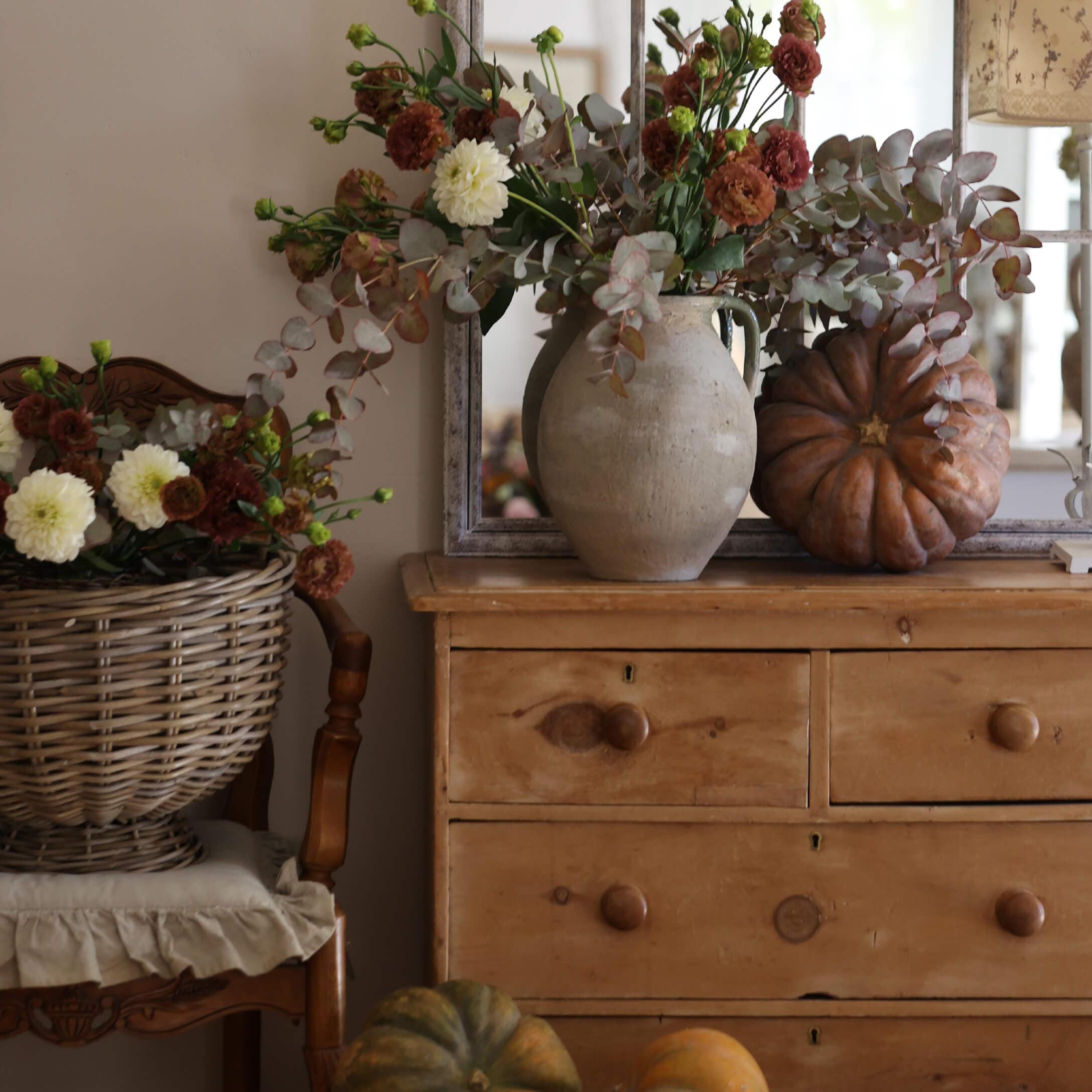 Commode en bois rustique avec vase en argile, bouquet d'automne et citrouilles décoratives dans un intérieur chaleureux