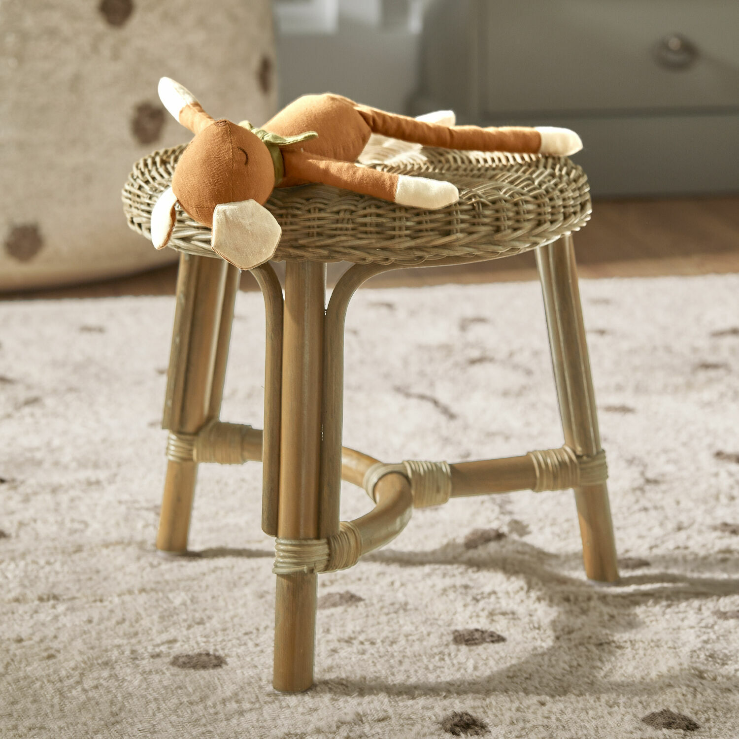 Tabouret Dunley Tabouret en rotin naturel avec peluche posée sur un tapis doux dans une chambre d'enfant