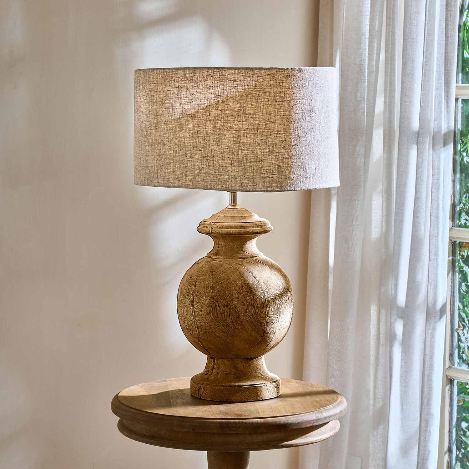 Lampe de table avec base en bois et abat-jour beige sur une table ronde près d'une fenêtre