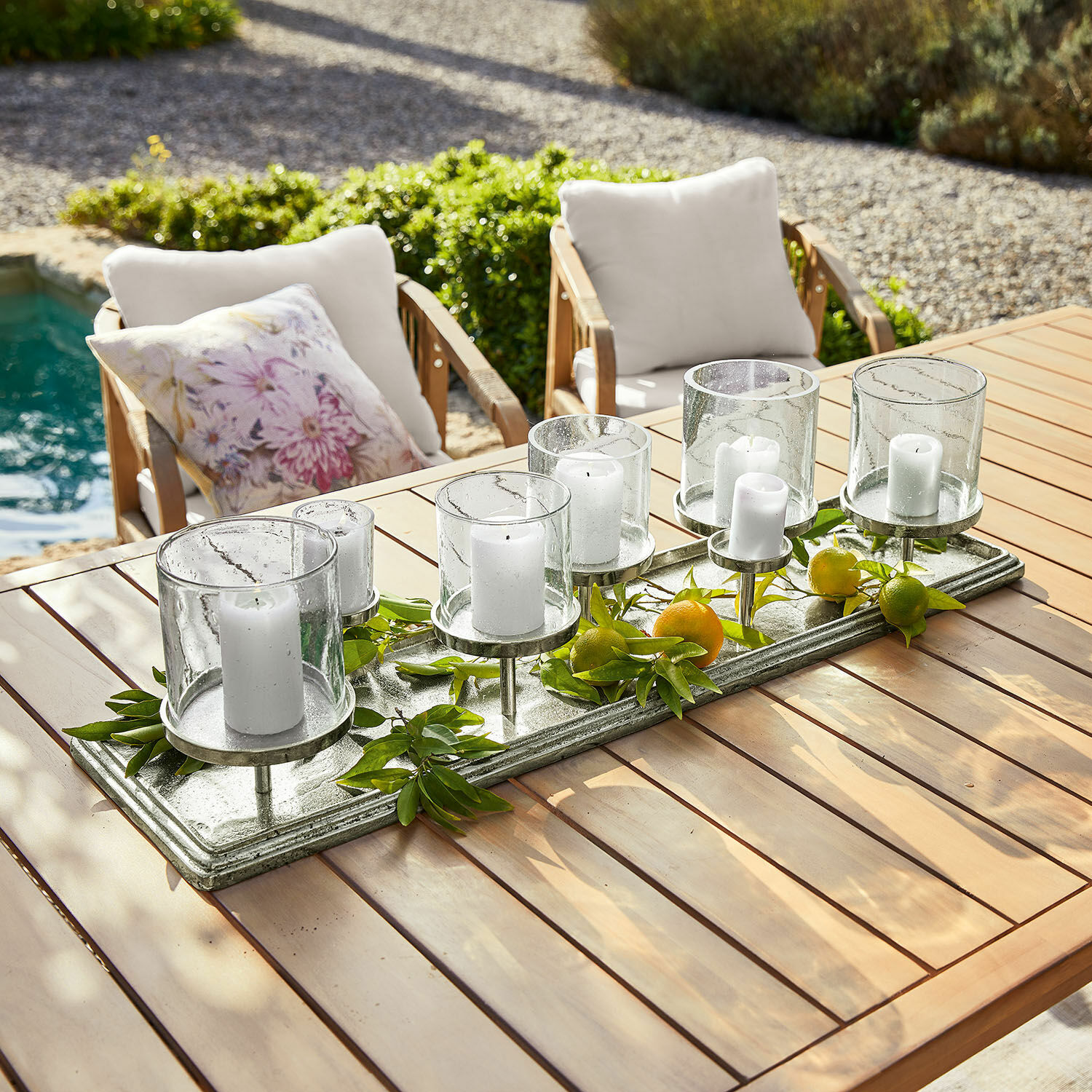Plateau à bougies Devonne Bougeoir décoratif en verre et métal avec bougies blanches sur table en bois dans un jardin
