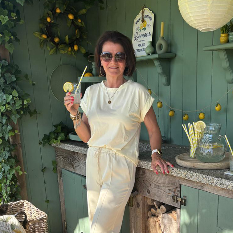 Femme en tenue crème se détend avec une limonade devant un mur vert décoré de citrons