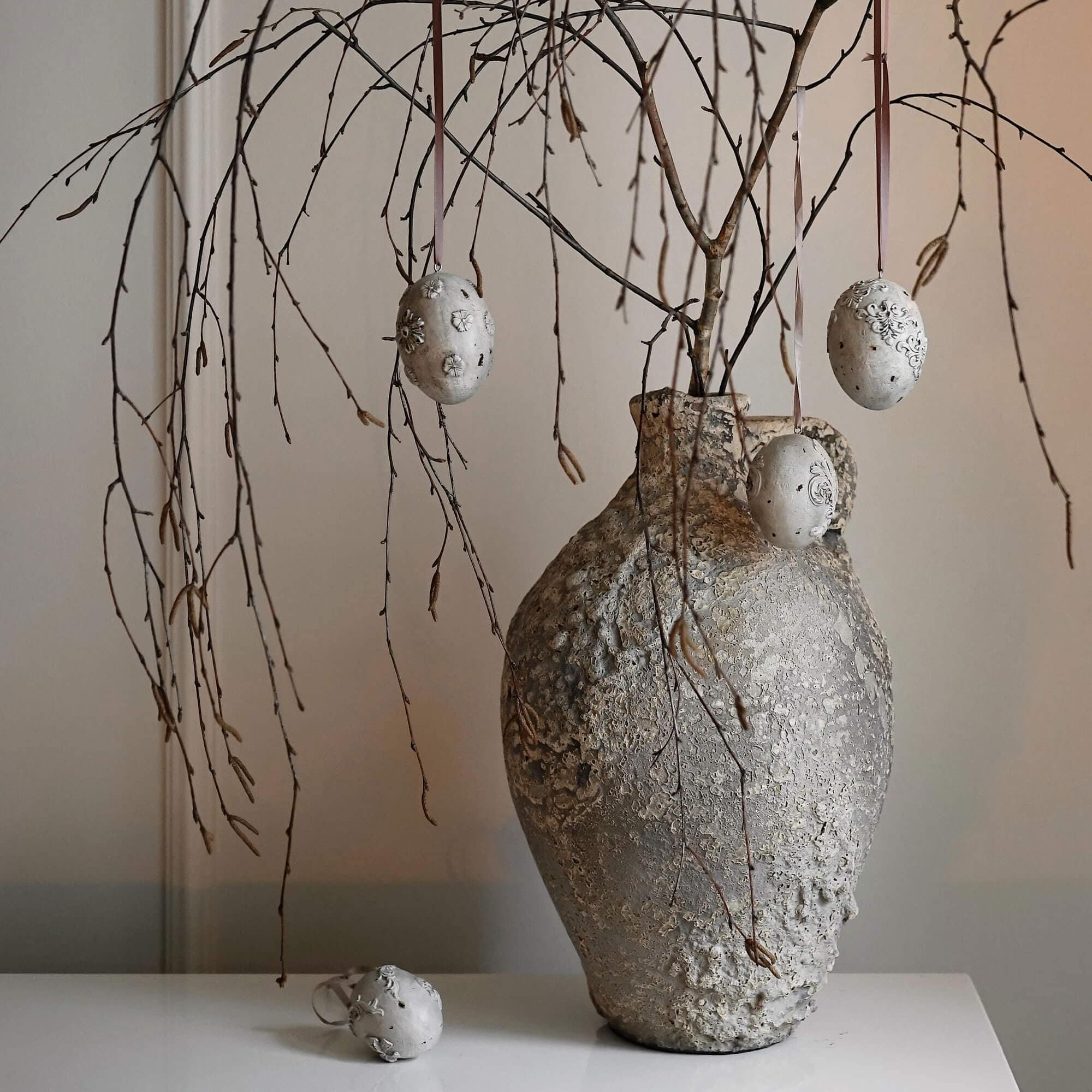 Vase rustique gris texturé avec branches et décorations suspendues en forme d'œufs décoratifs